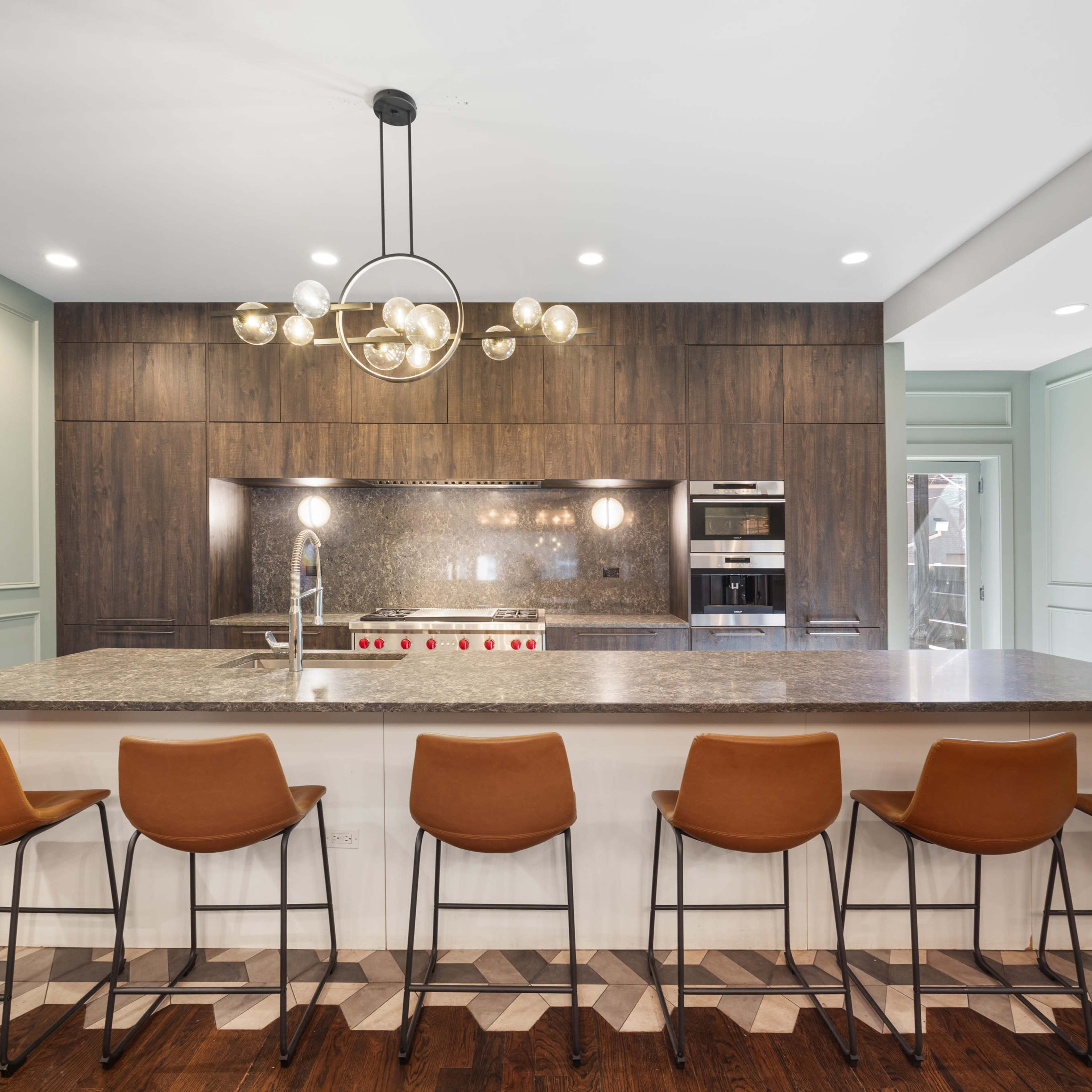 A modern kitchen features a central island with seating for six, surrounded by wood-paneled cabinetry and equipped with stainless steel appliances.