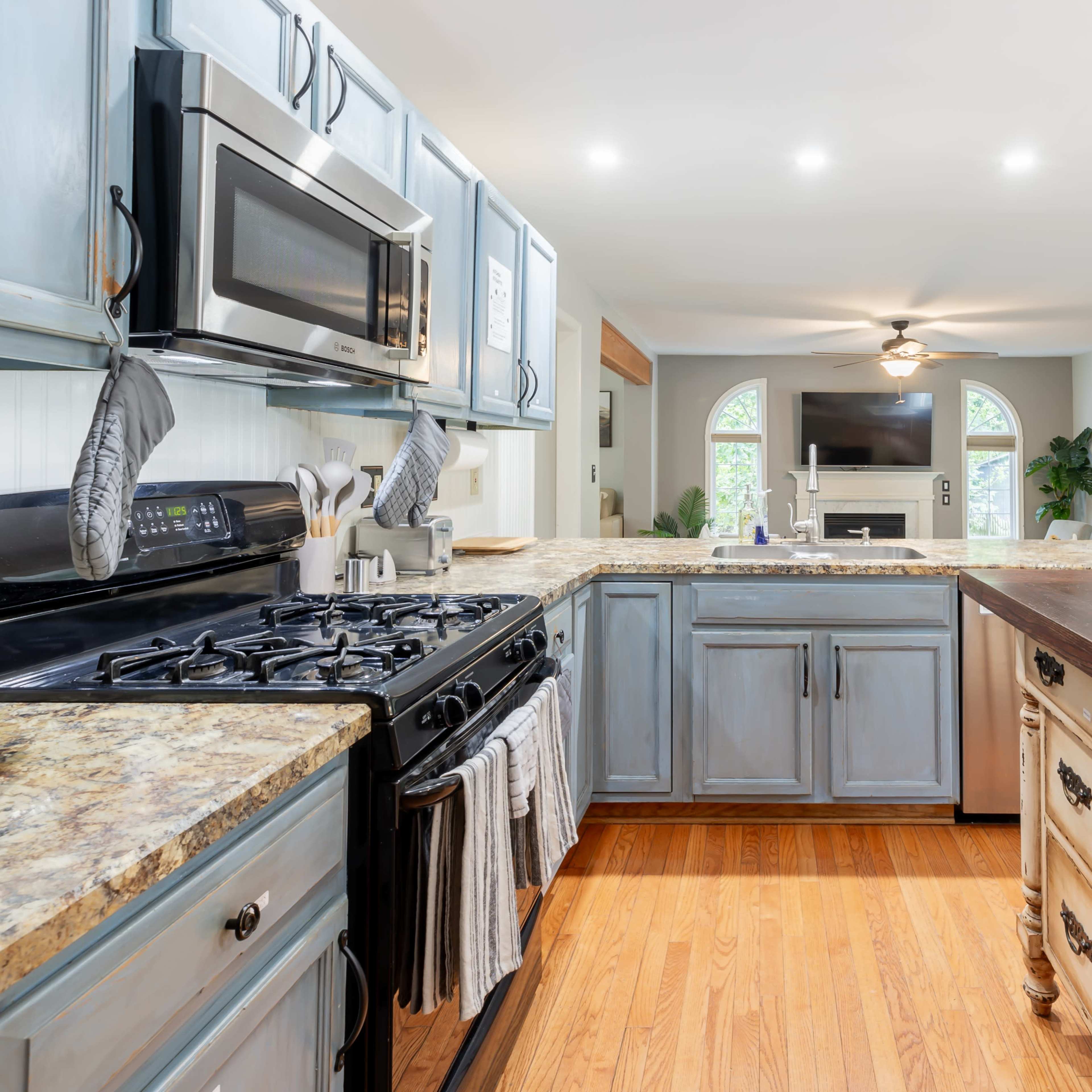 A modern kitchen featuring a blend of blue cabinets and a wooden island with a countertop, equipped with stainless steel appliances and an open layout leading to a living area.