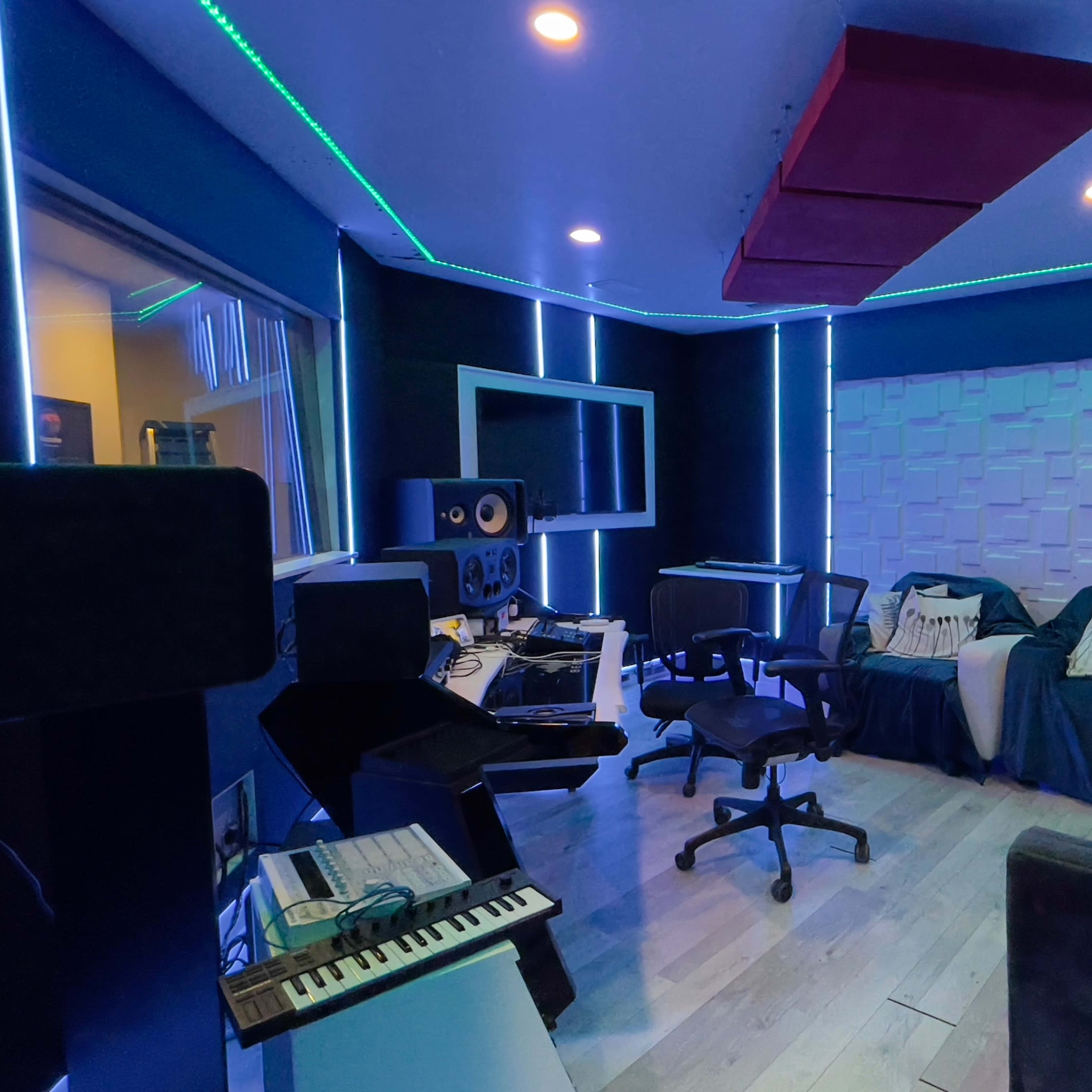 A music studio interior features a mixing area with equipment, a lounge area with couches, and ambient LED lighting along the walls.