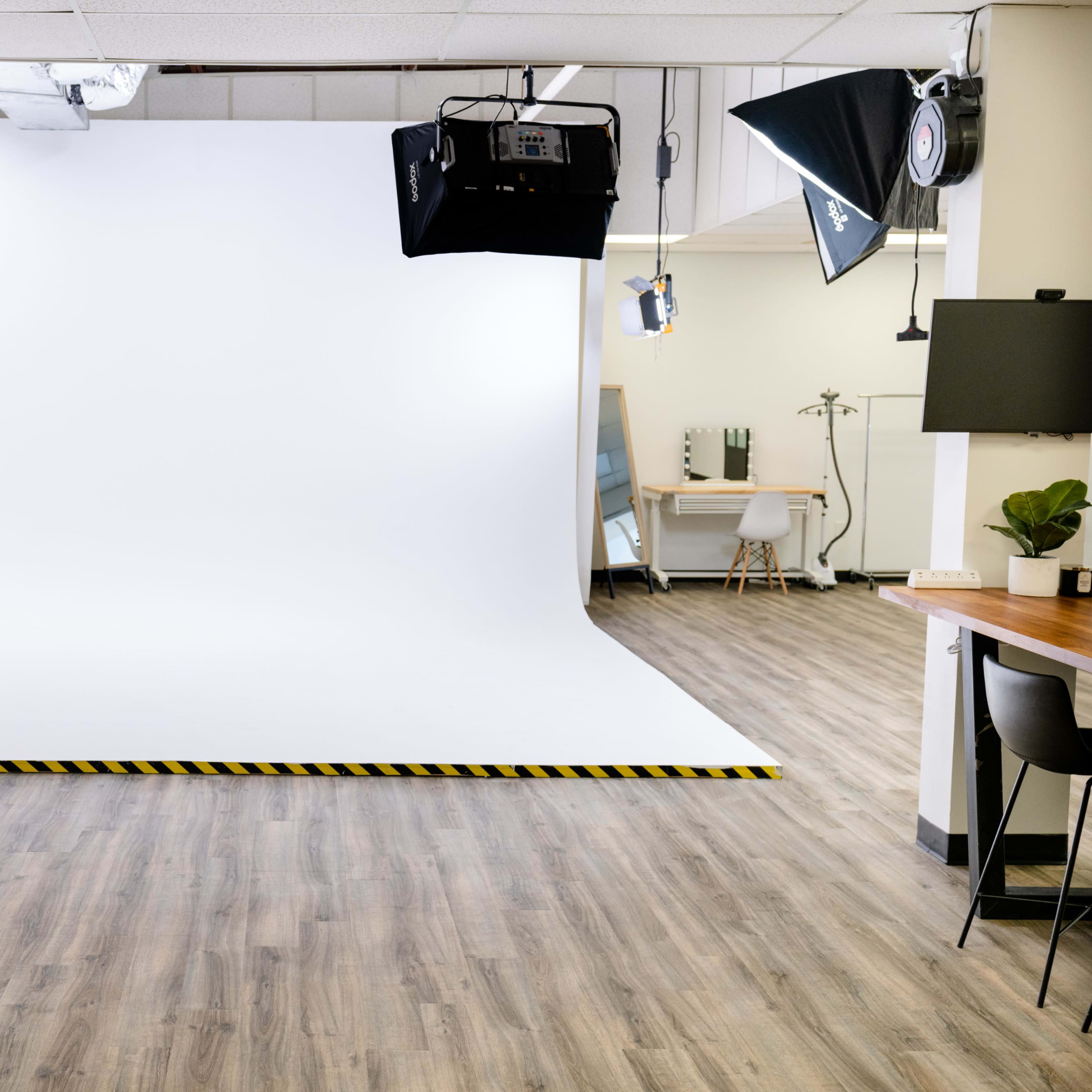 A photography studio with a white backdrop, spotlights, and wooden flooring.
