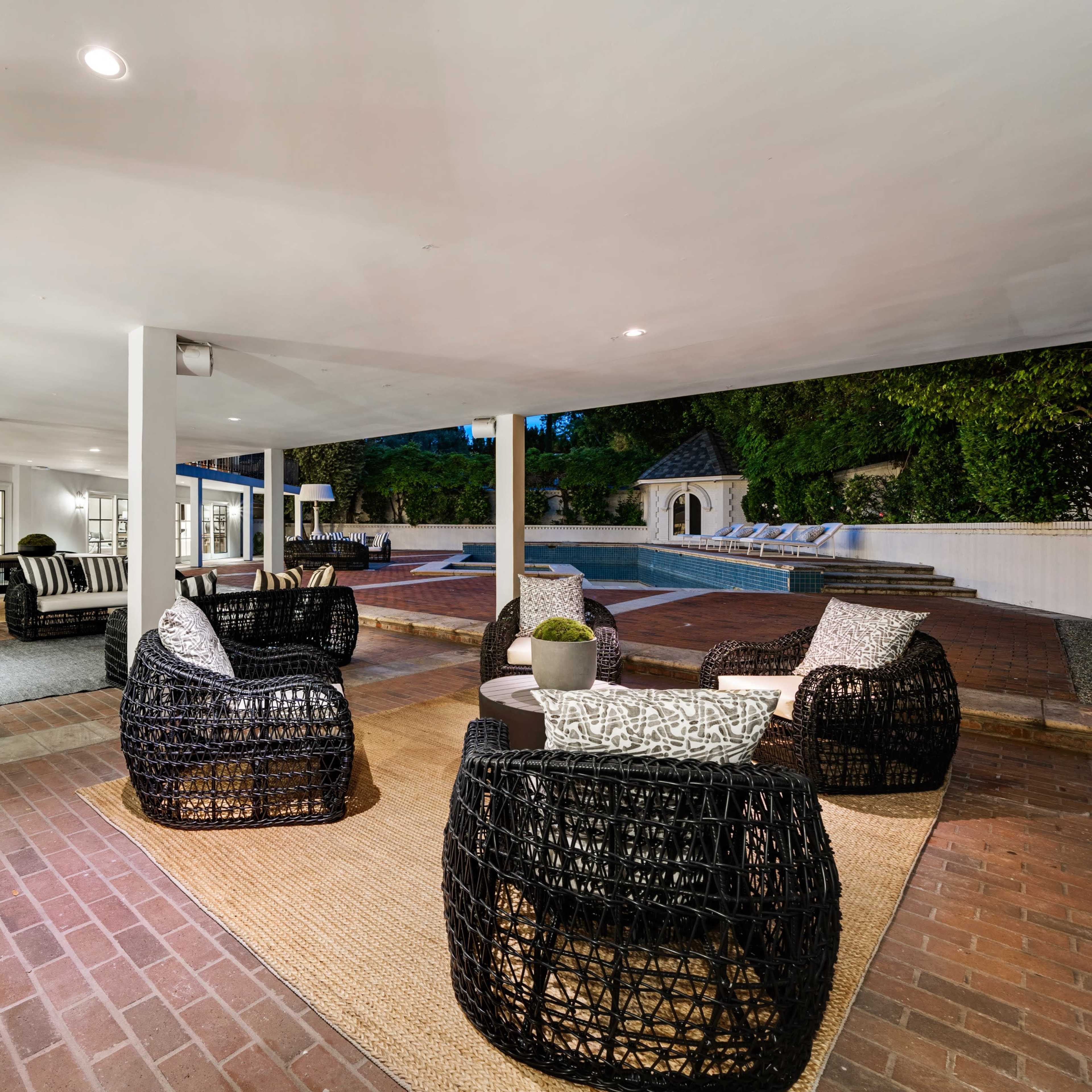A spacious outdoor patio area with woven chairs arranged around a central table, leading to a swimming pool in the background.