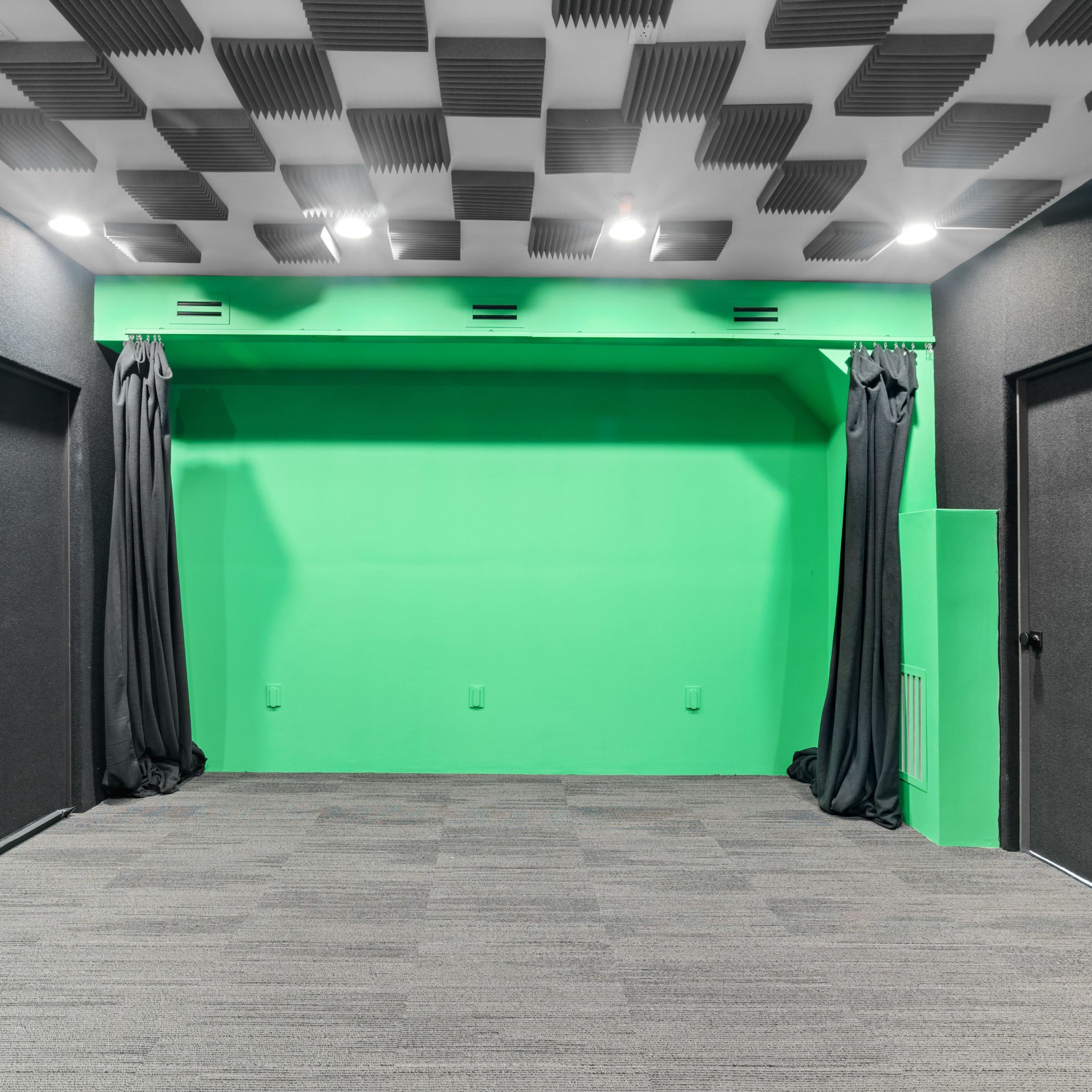 A soundproofed room with a green screen backdrop, two dark doors, and a carpeted floor.