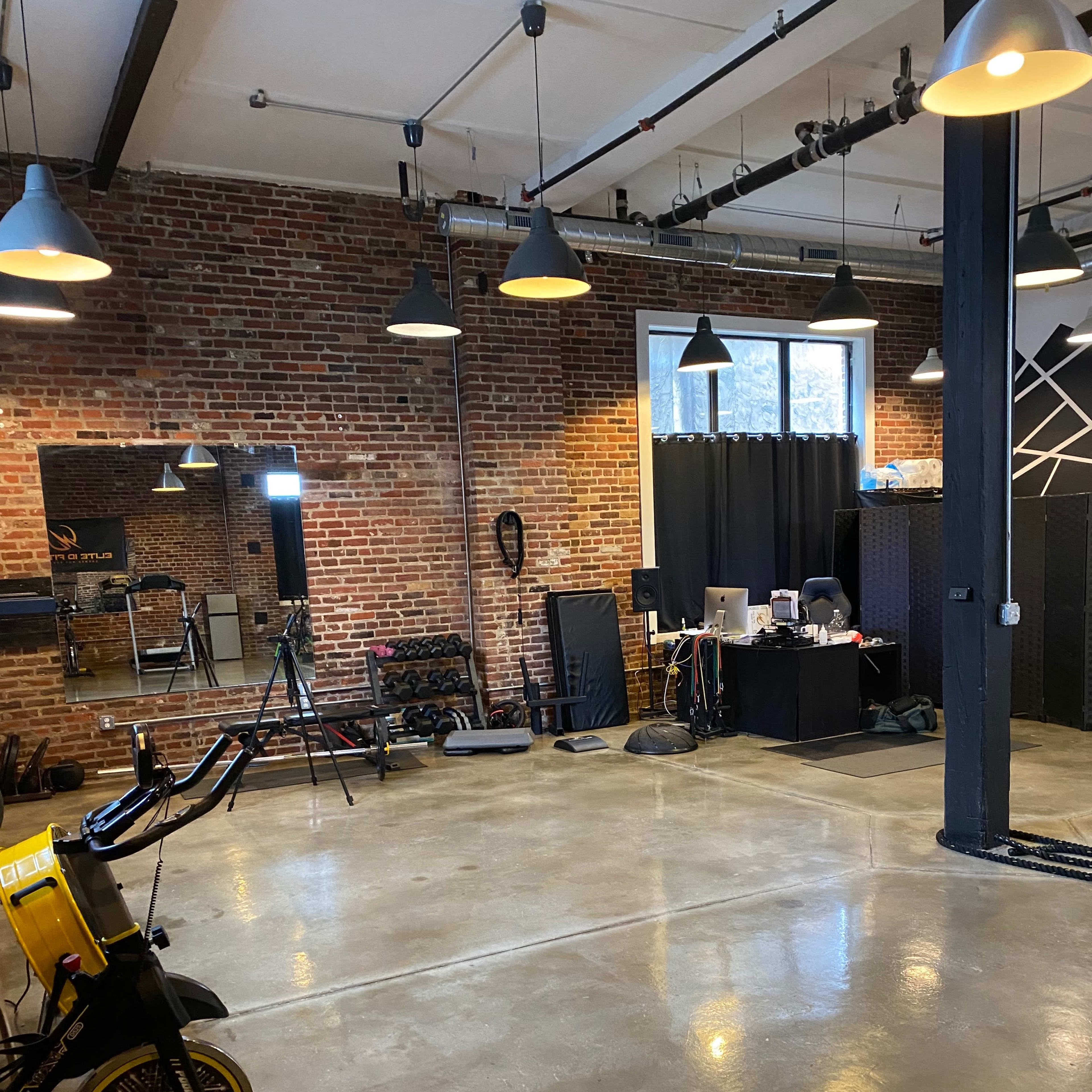 A spacious gym with brick walls, exercise equipment, and a desk area with a computer.