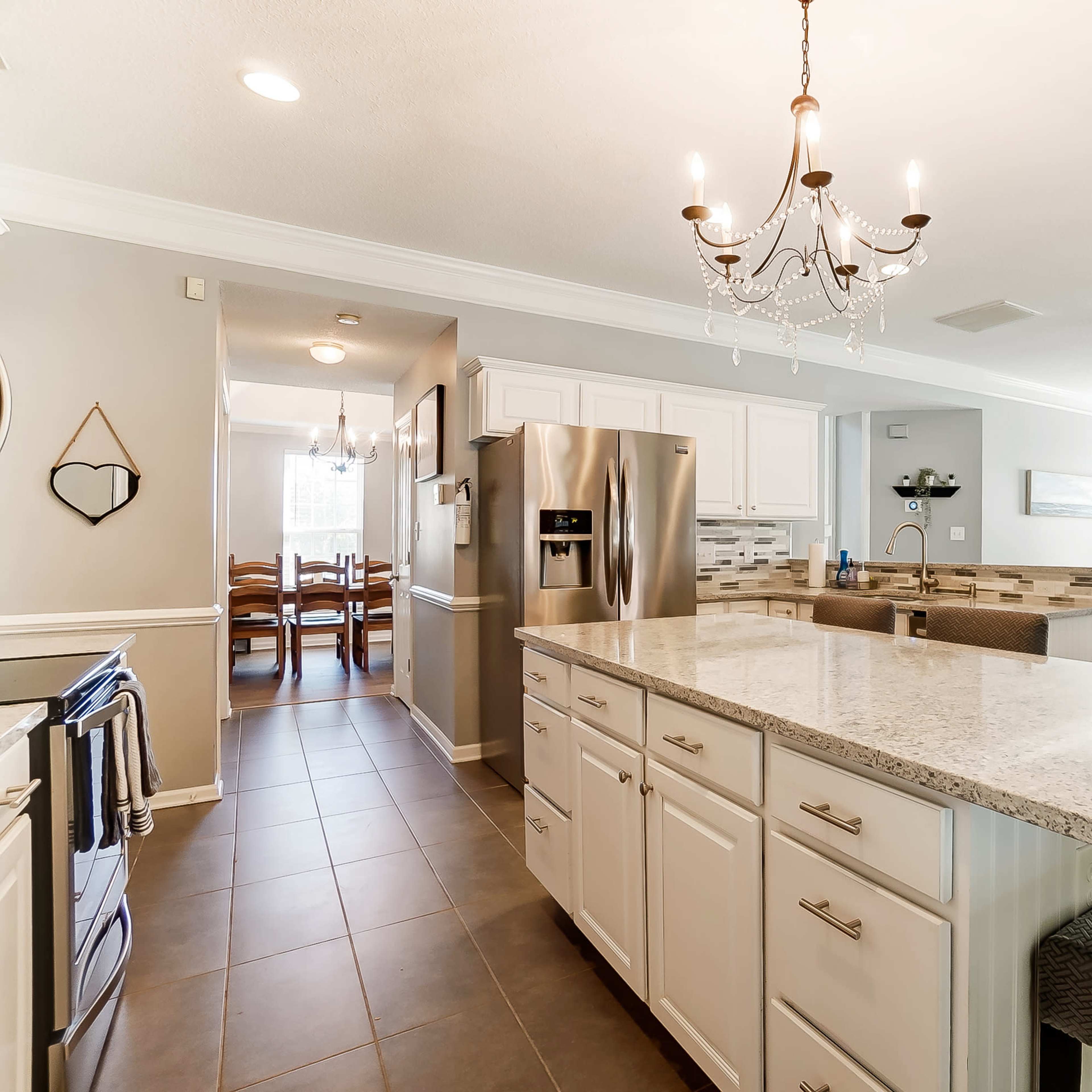 A modern kitchen with white cabinetry, a granite island with seating, and an open layout leading to a living area.