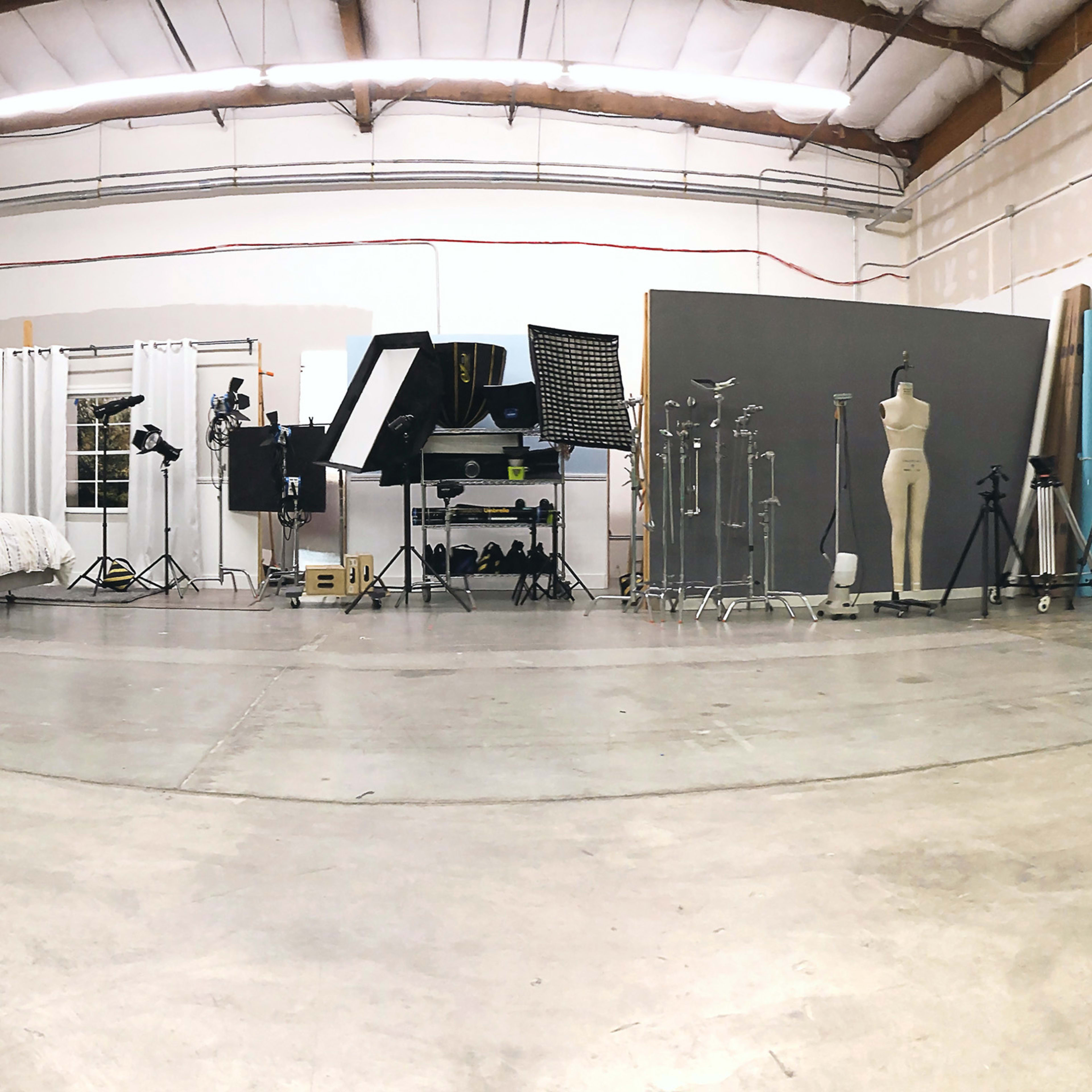 A spacious photography studio with various backdrops, lighting equipment, and a bed set up against one wall.