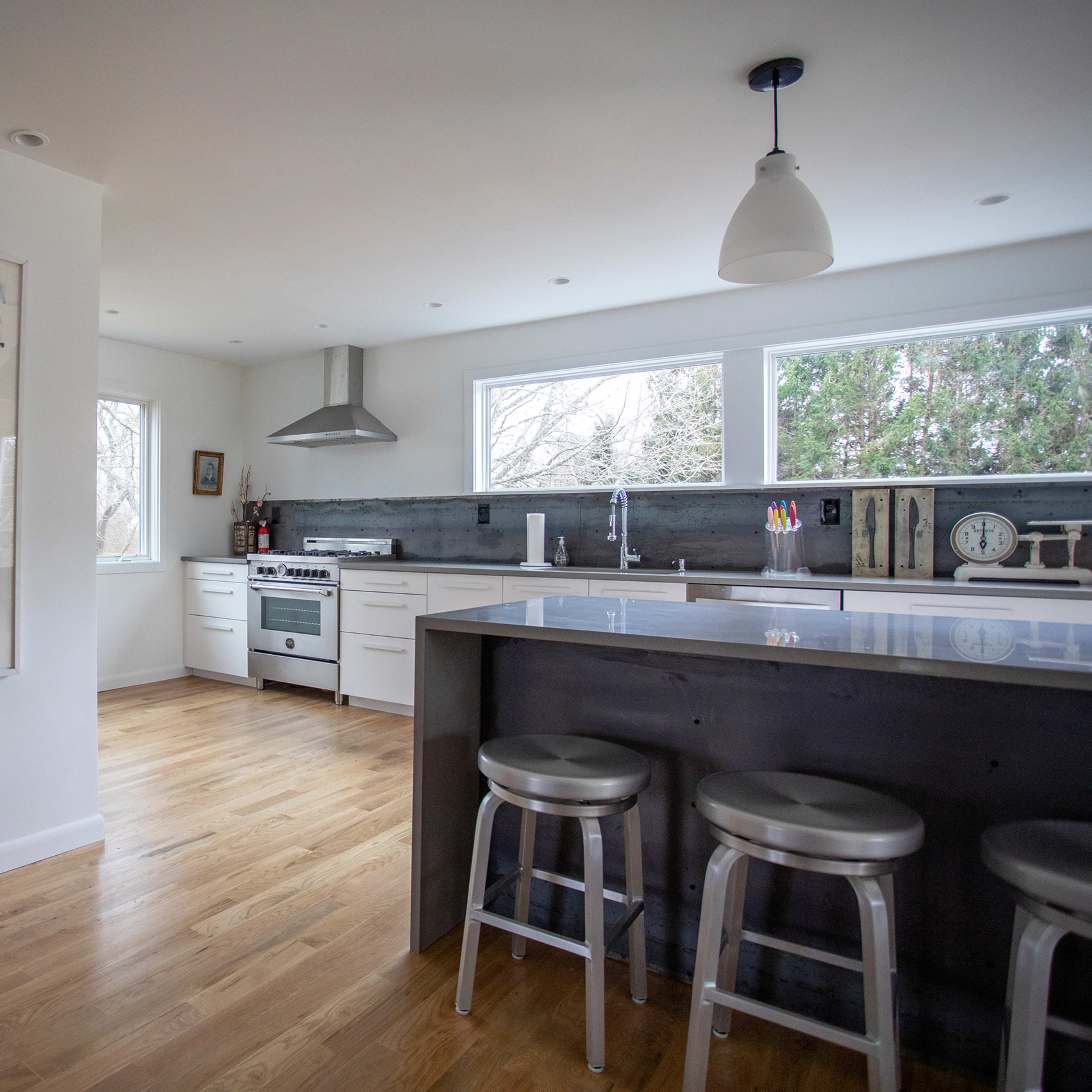 A modern kitchen with stainless steel appliances, a central island with bar stools, and large windows letting in natural light.