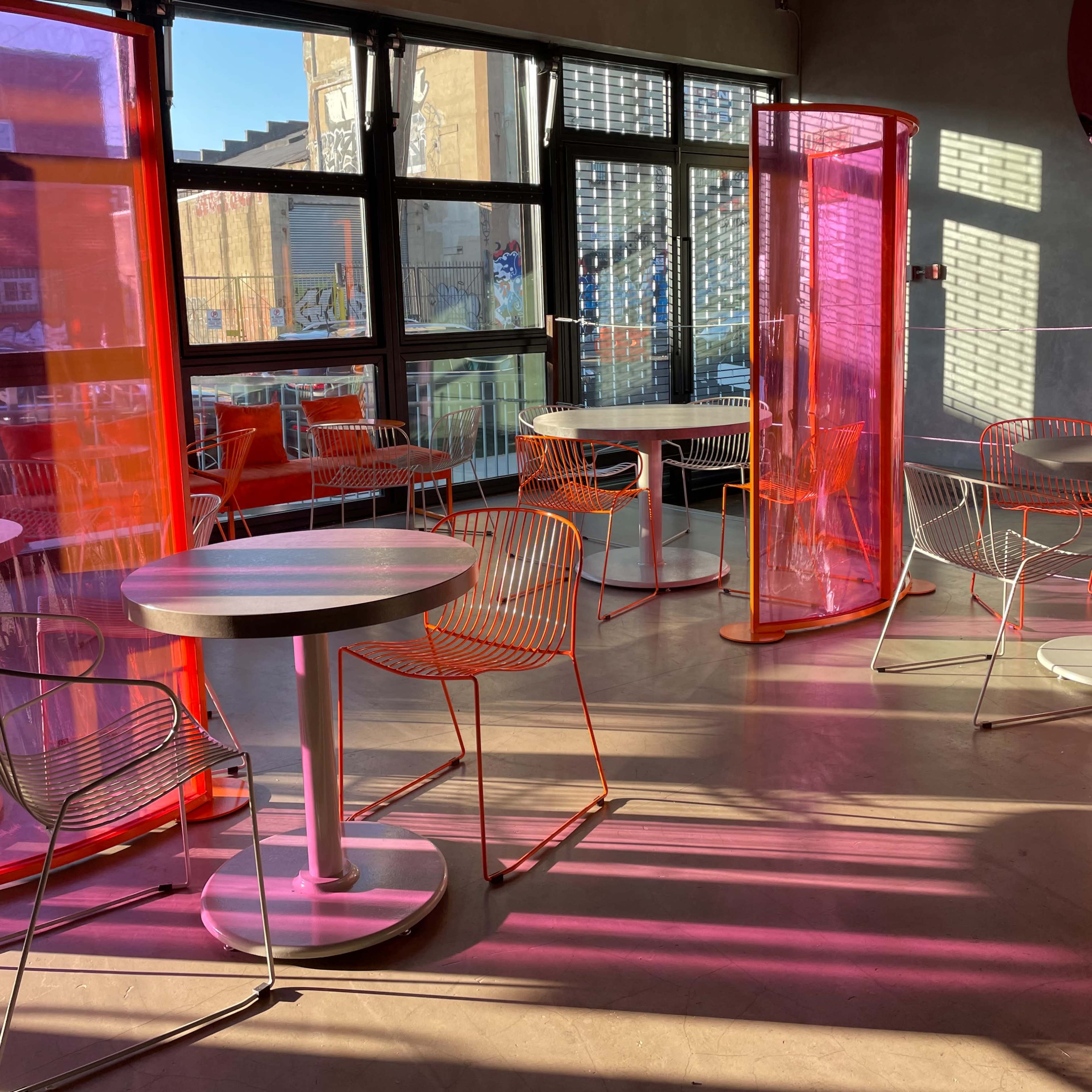 A modern café interior with colorful translucent partitions, empty tables, and sunlight casting shadows across the floor.