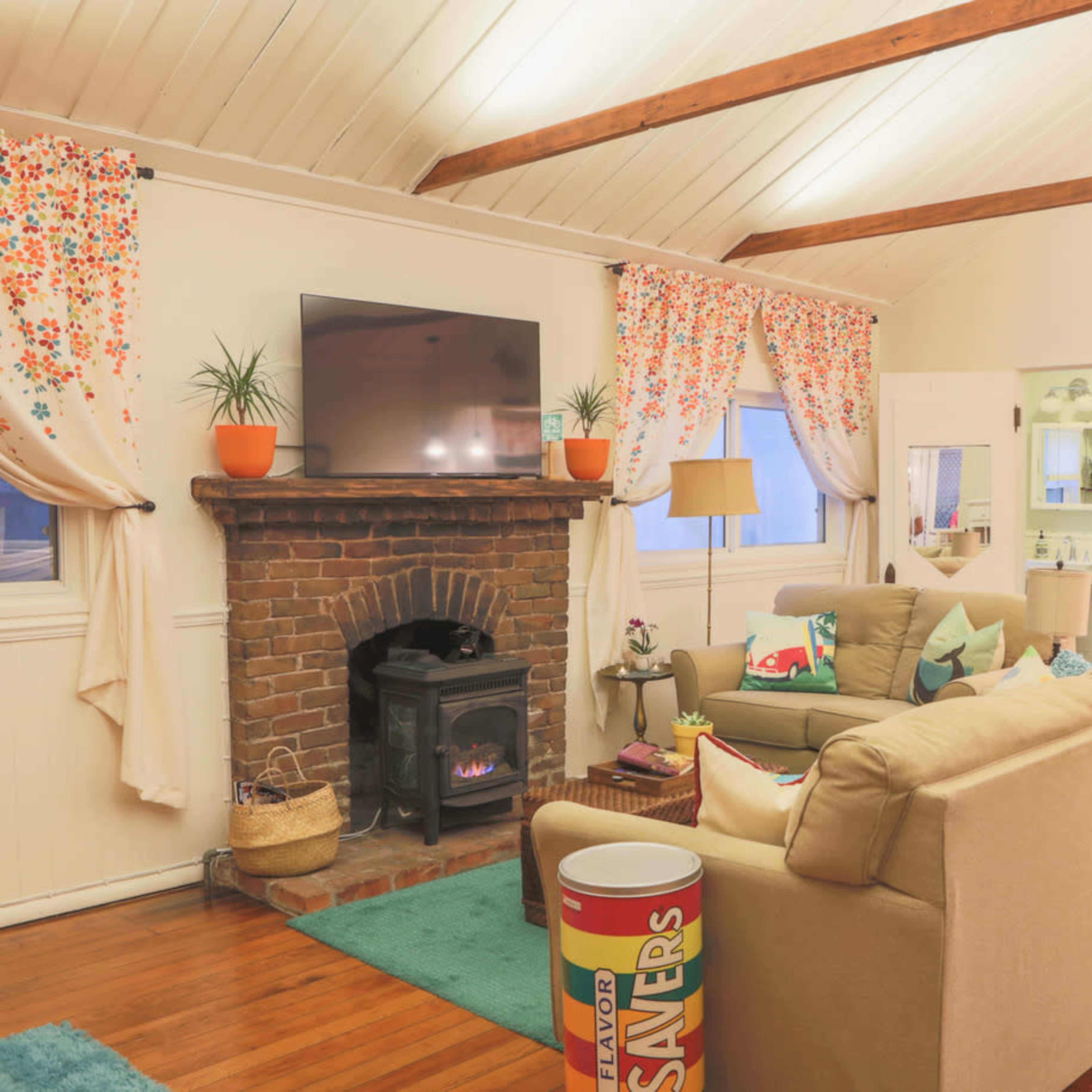 A cozy living room with a brick fireplace, a television mounted on the wall, and a sofa arranged around a small table.