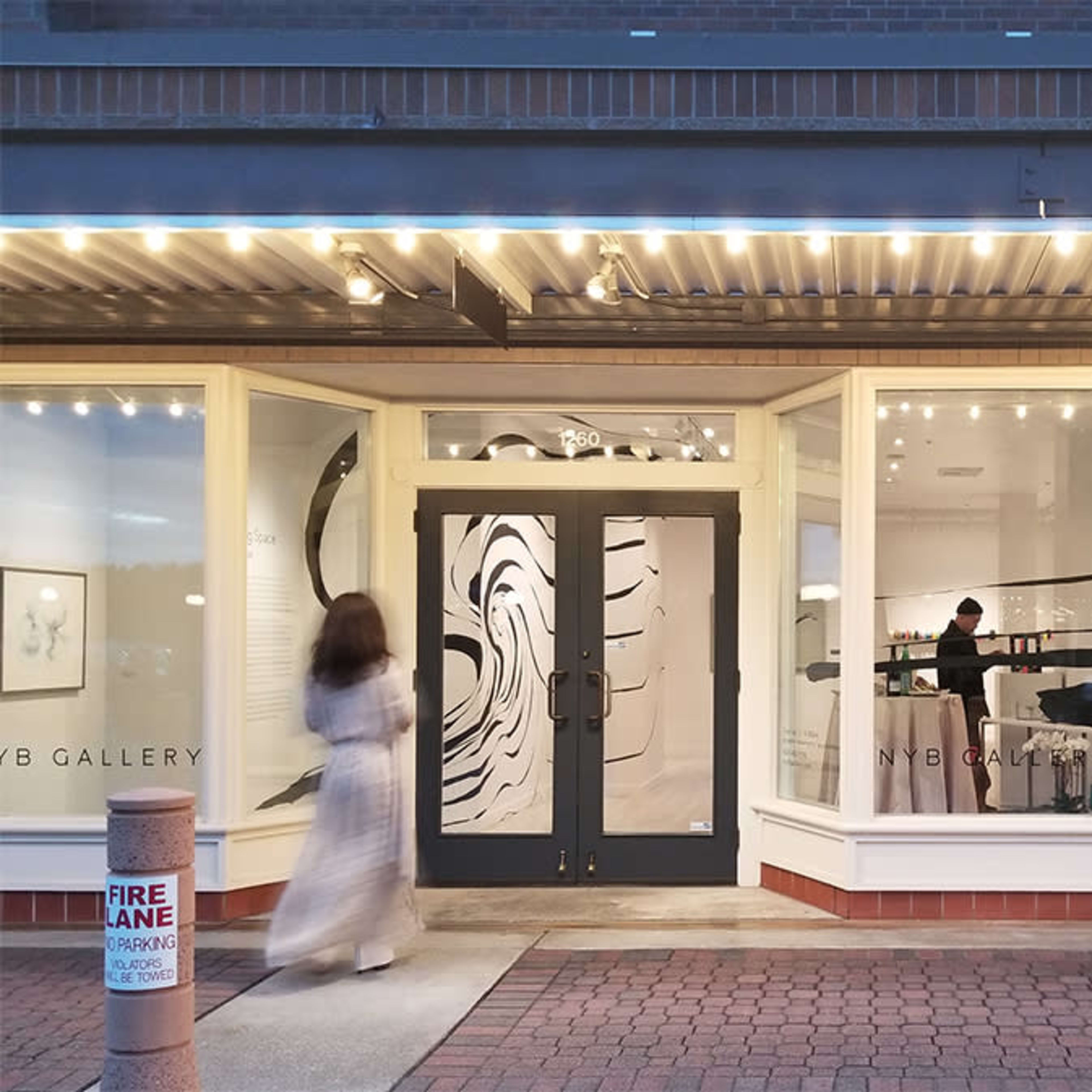 A person walks past the entrance of the NYB Gallery, which features large, abstract artwork displayed in its windows.
