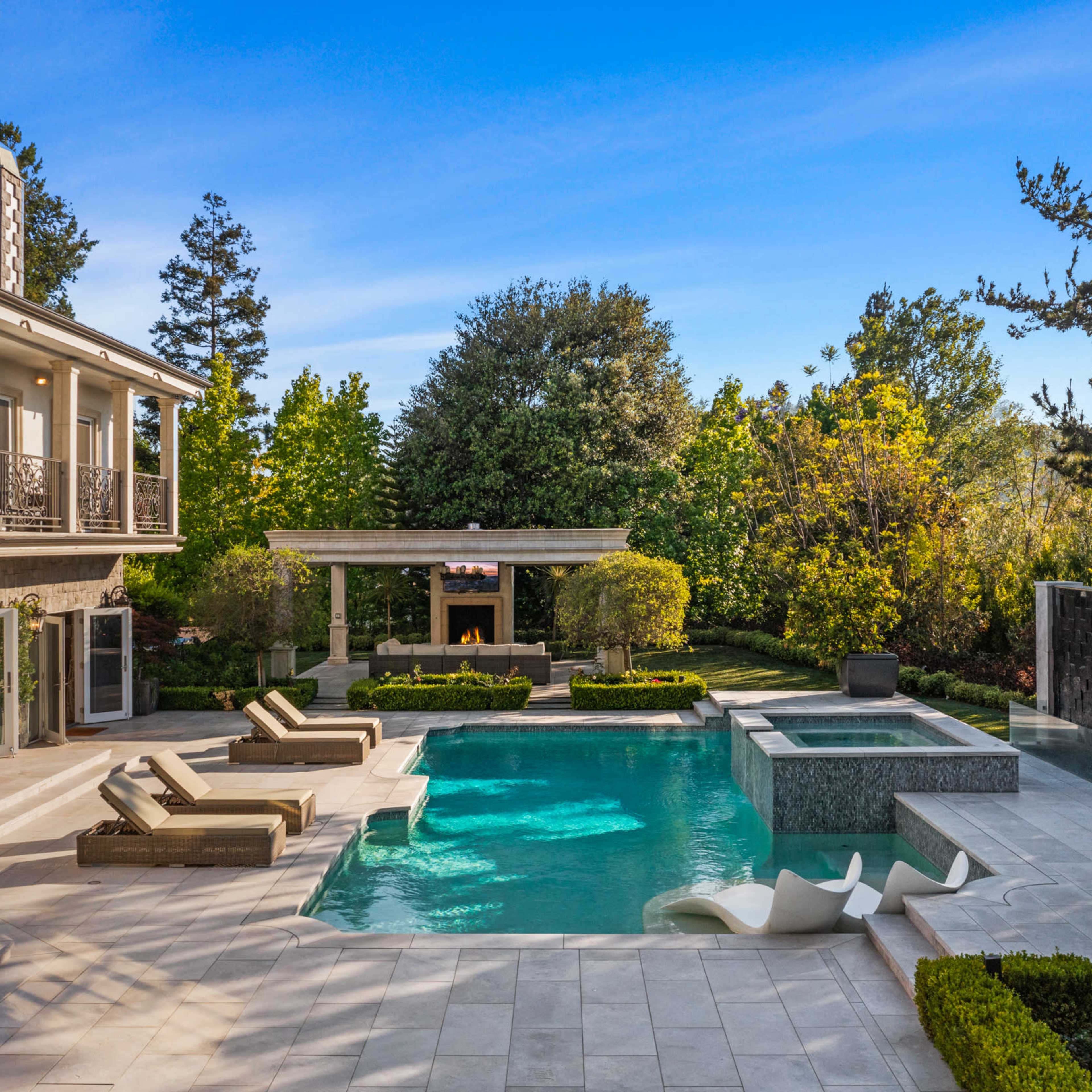A luxurious residential backyard with a swimming pool, spa, outdoor seating area, and well-manicured landscaping.