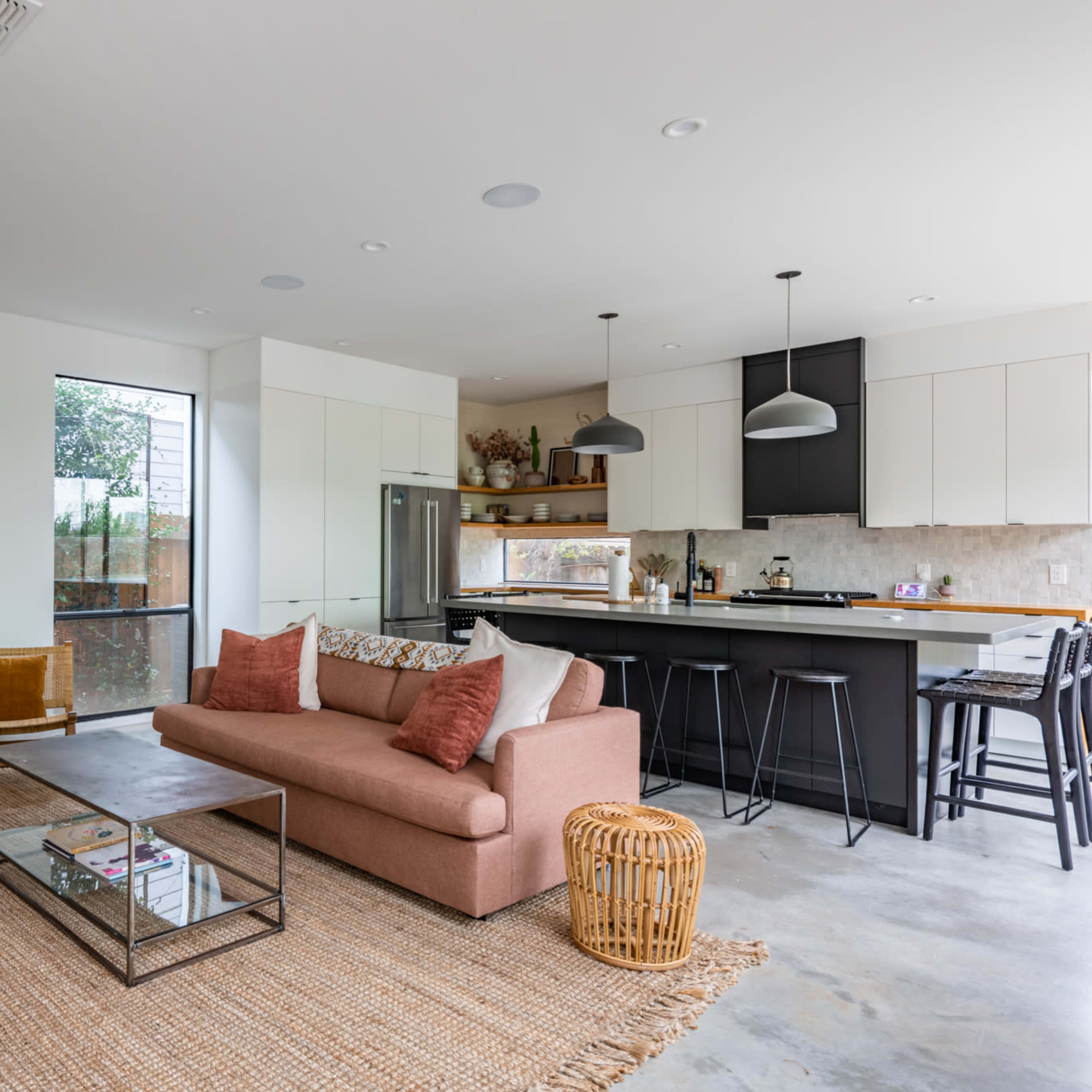 A modern living room features a pink sofa, a glass coffee table, and wooden furniture, with an open kitchen visible in the background.