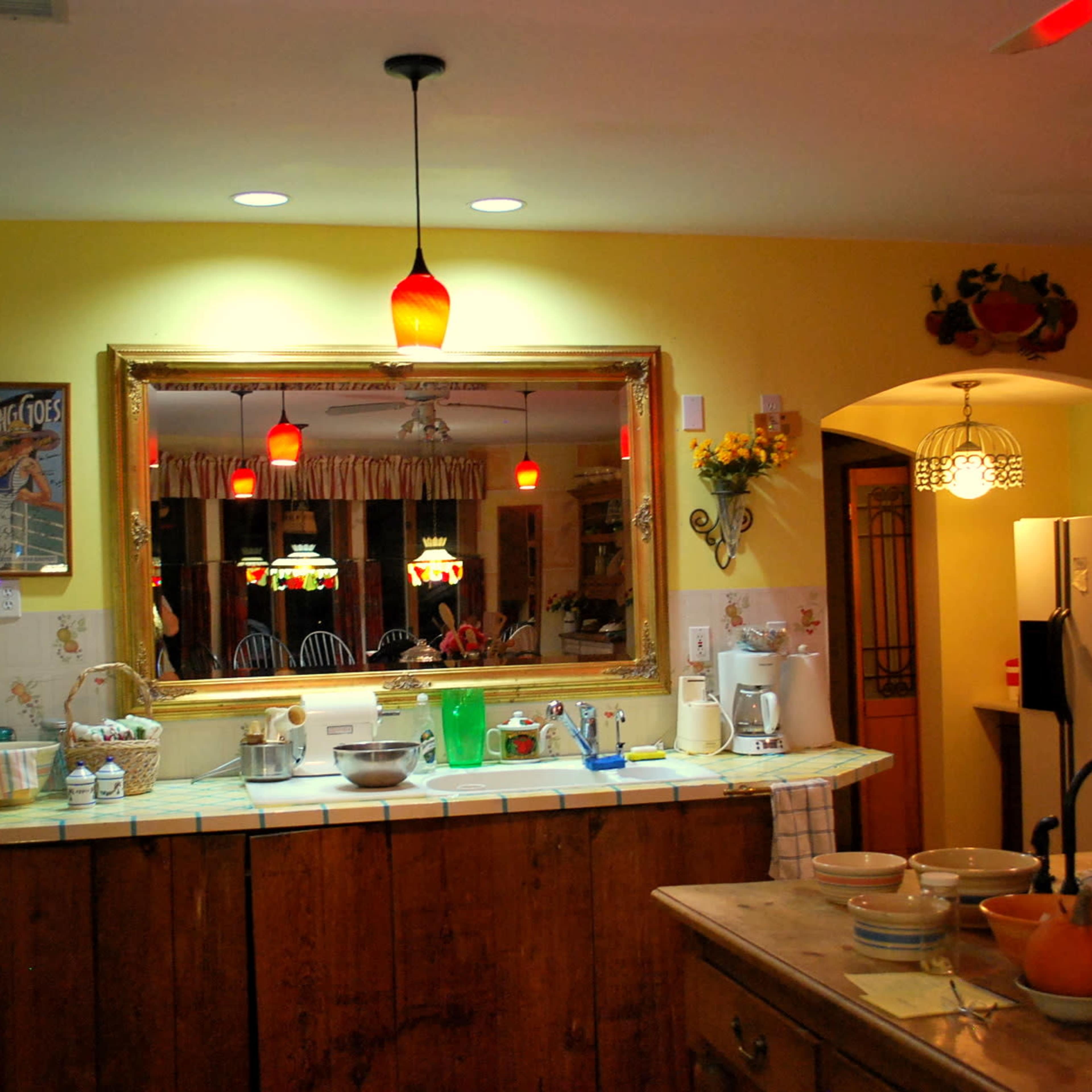 A warmly lit kitchen featuring a wooden countertop, a large mirror, and various appliances and utensils arranged on the counter.