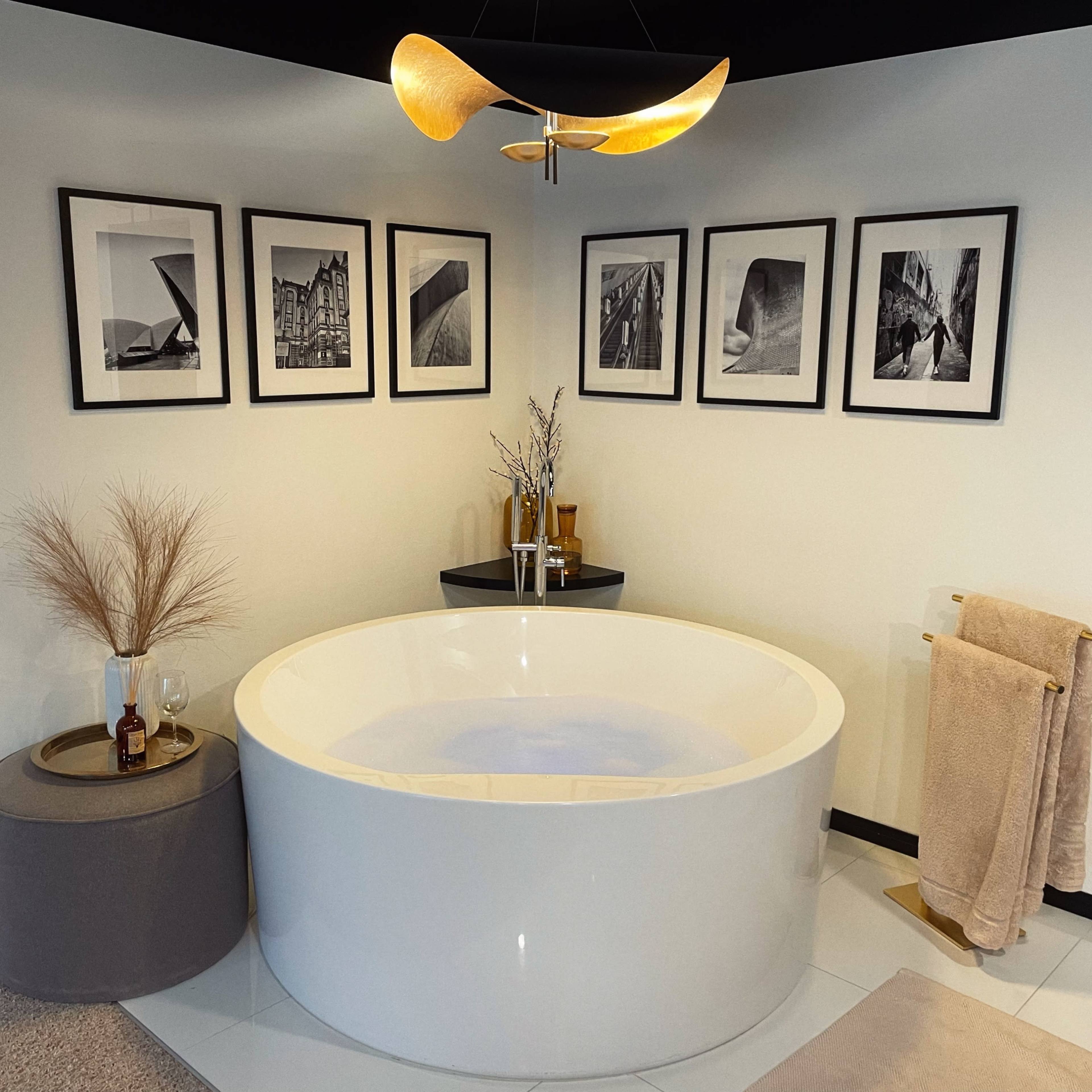 A modern bathroom featuring a circular white bathtub, framed black and white photographs on the wall, and decorative elements like a small plant and a towel rack.