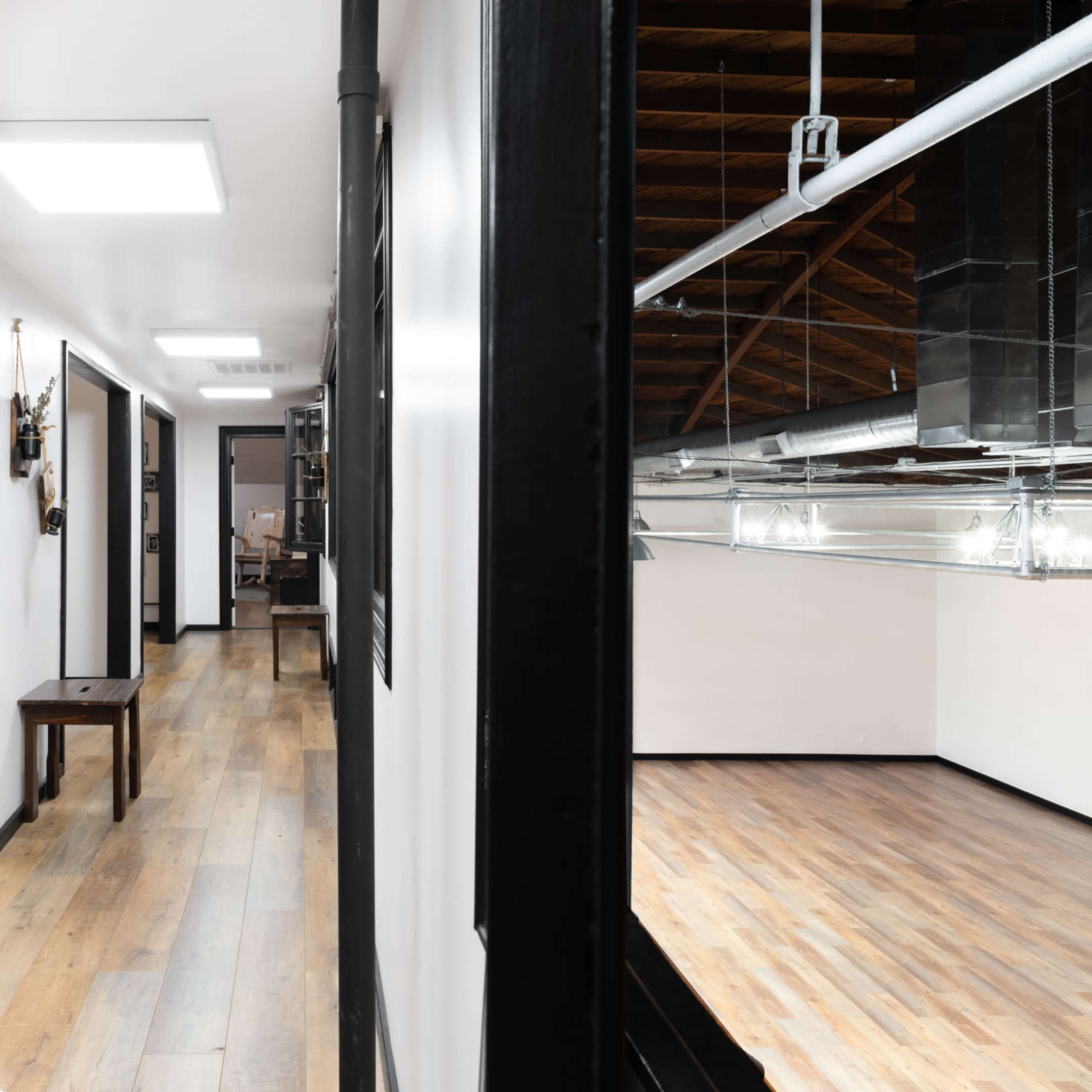 A spacious interior with wooden floors, exposed beams, and industrial lighting fixtures, viewed from a hallway.