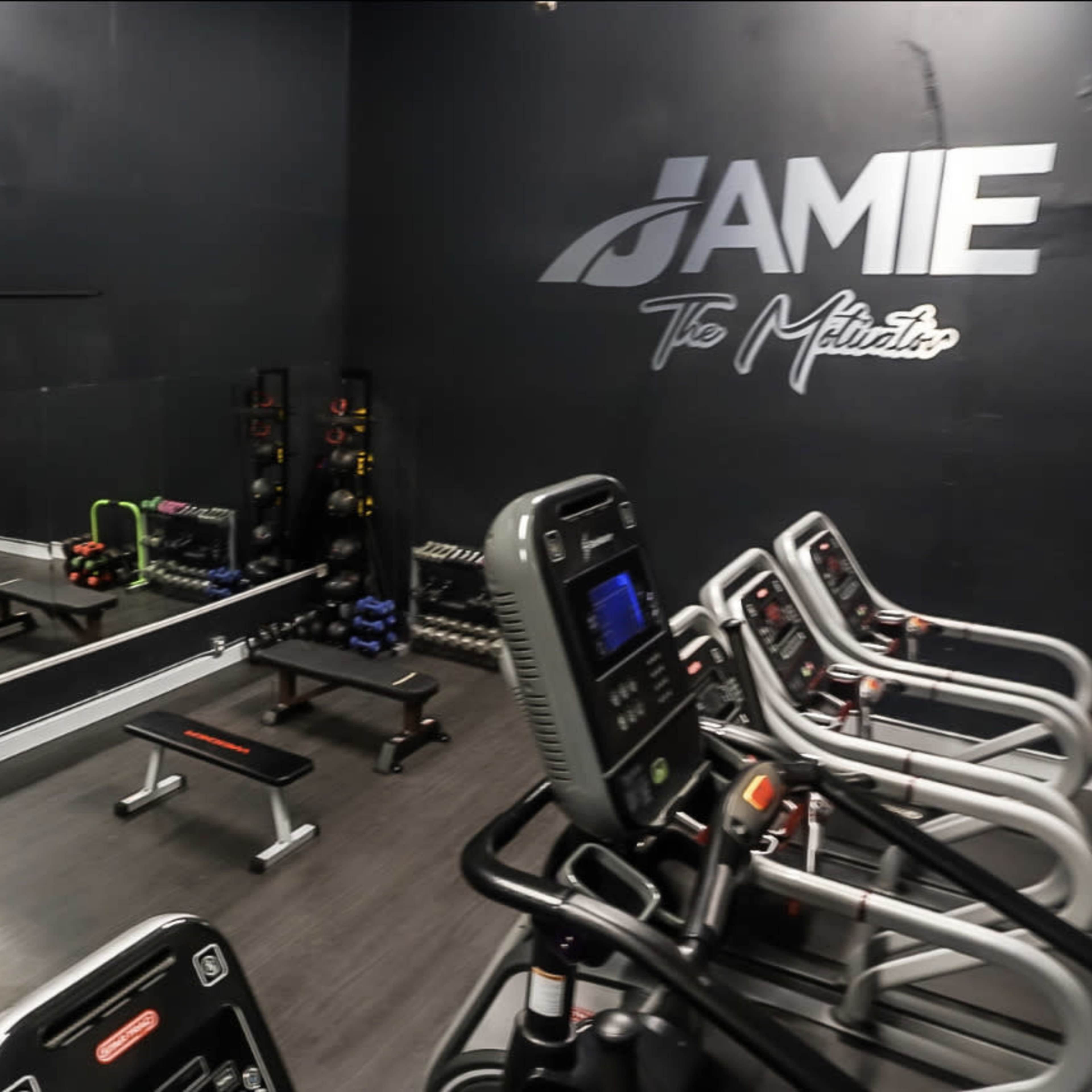 A small gym with exercise equipment, including benches, weights, and cardio machines, against a black wall.