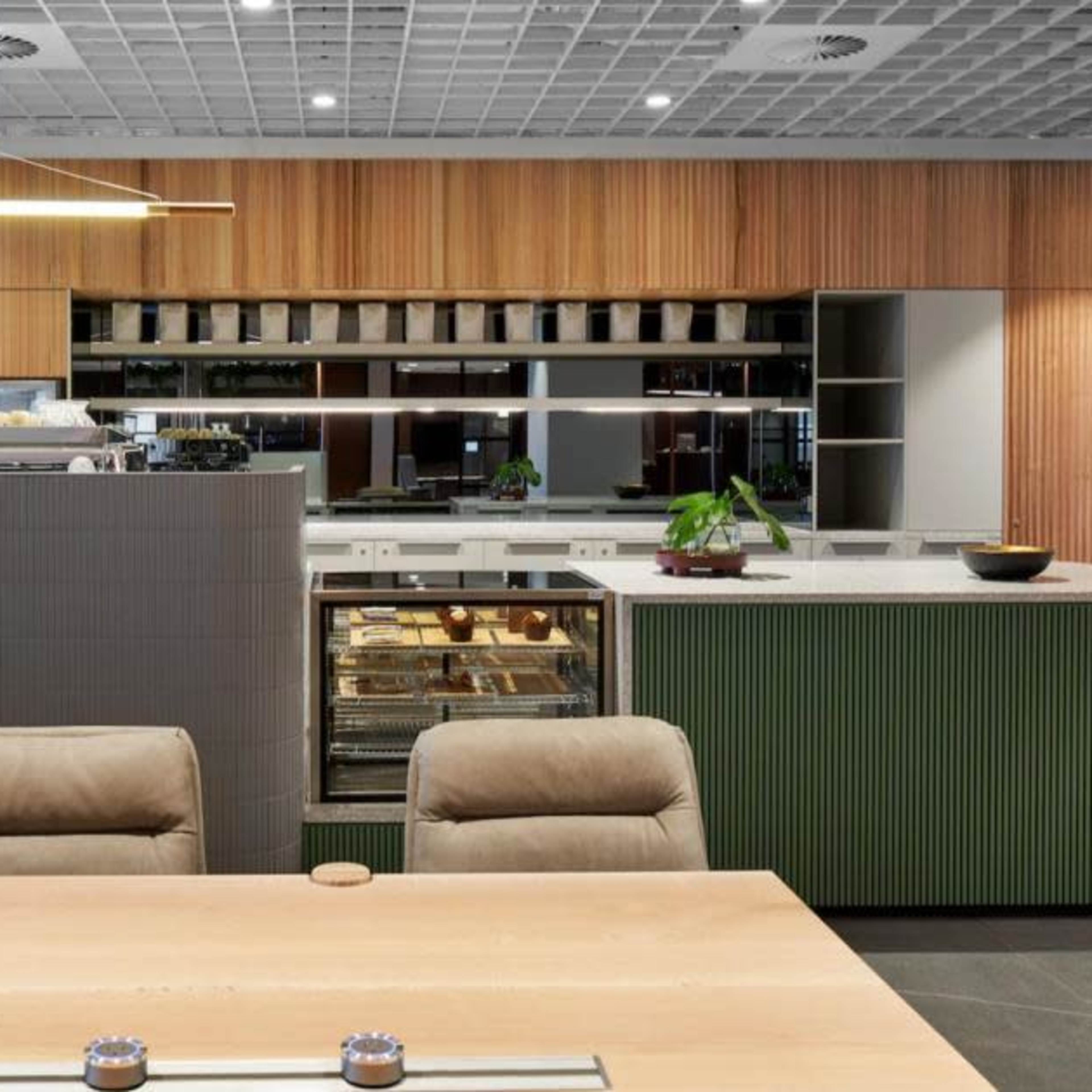 A modern kitchen with wooden cabinetry, a central island, and a dining table arranged with leather chairs.