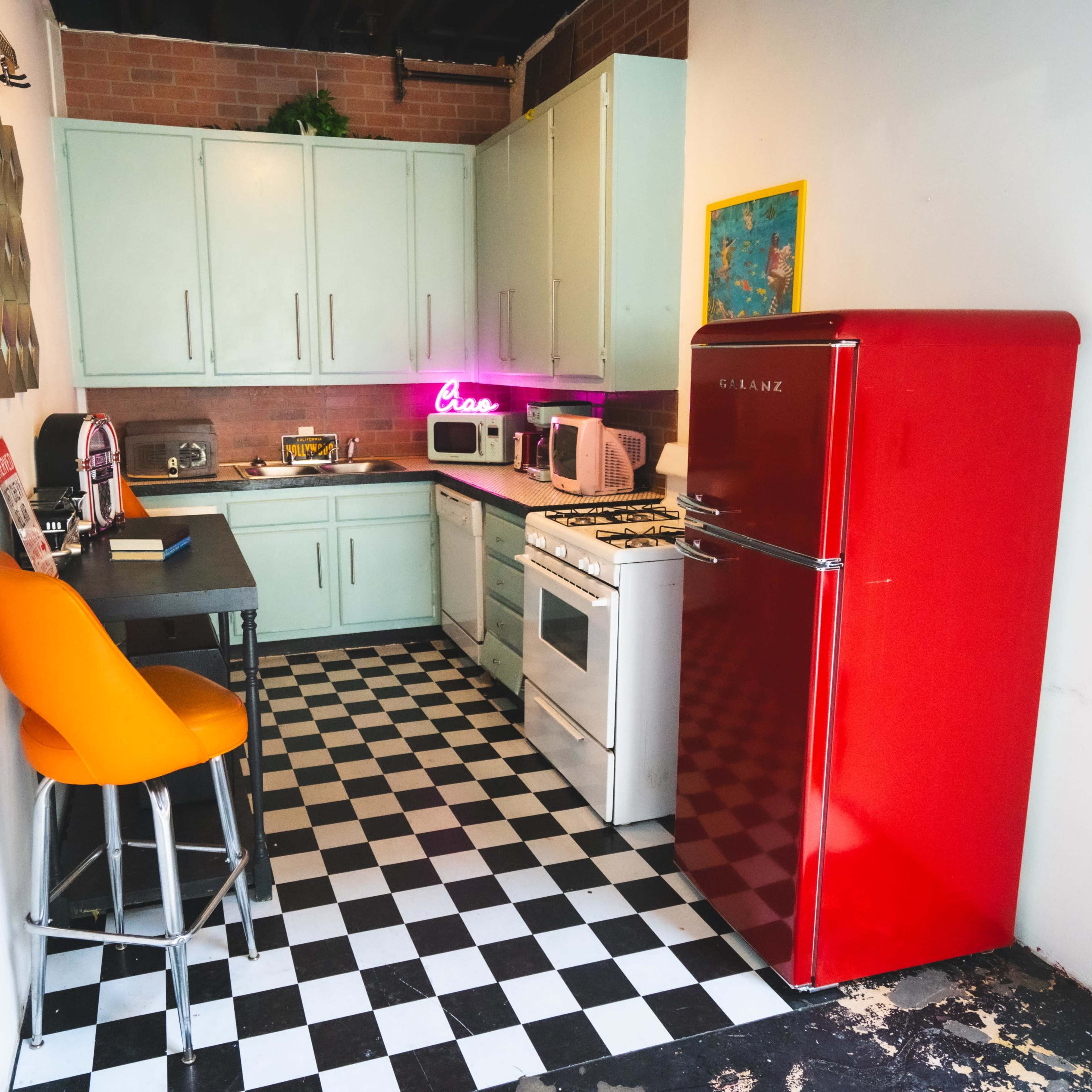 A compact kitchen features mint green cabinets, a red refrigerator, and a black-and-white checkered floor.