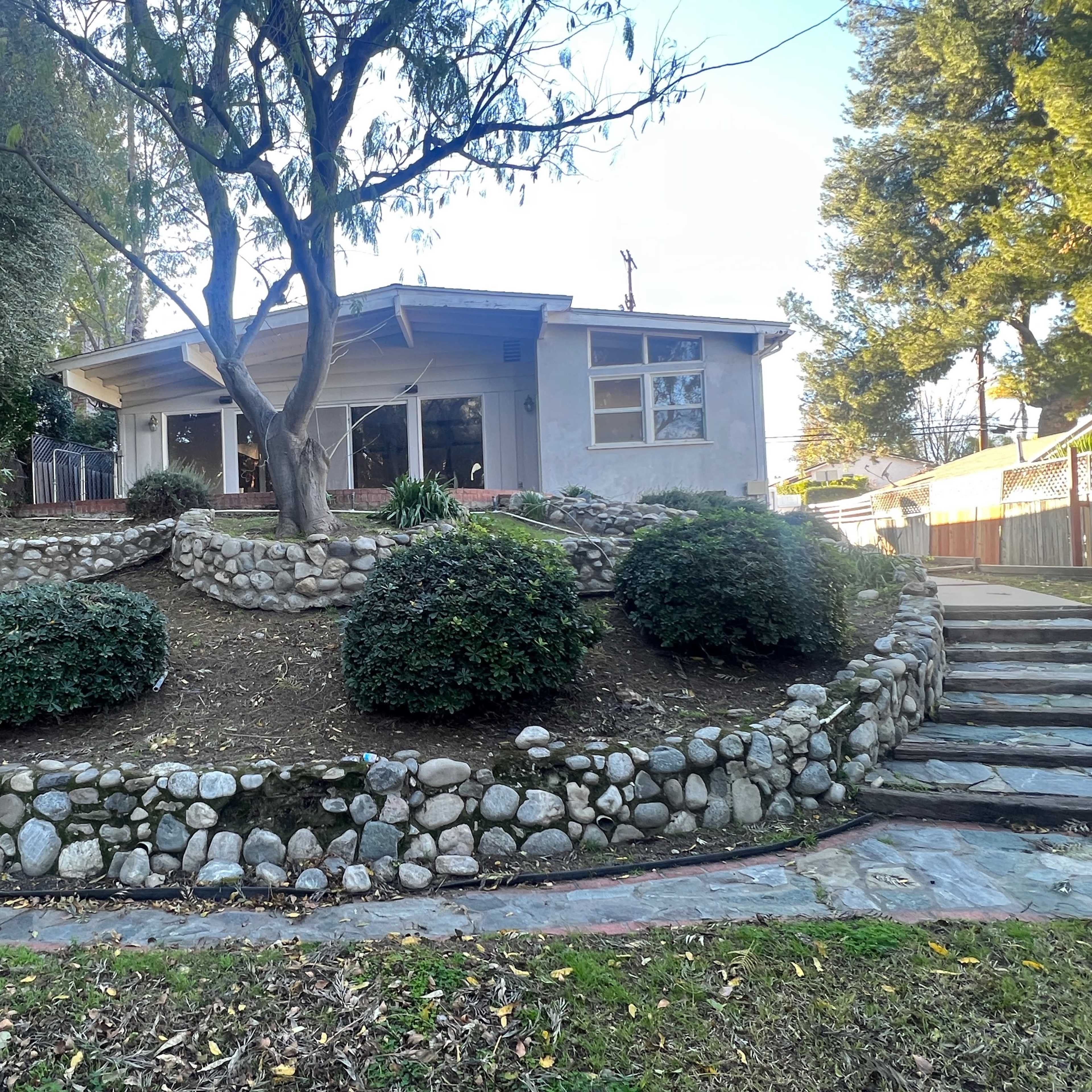A house with a stone garden featuring circular shrubbery, surrounded by steps and trees.