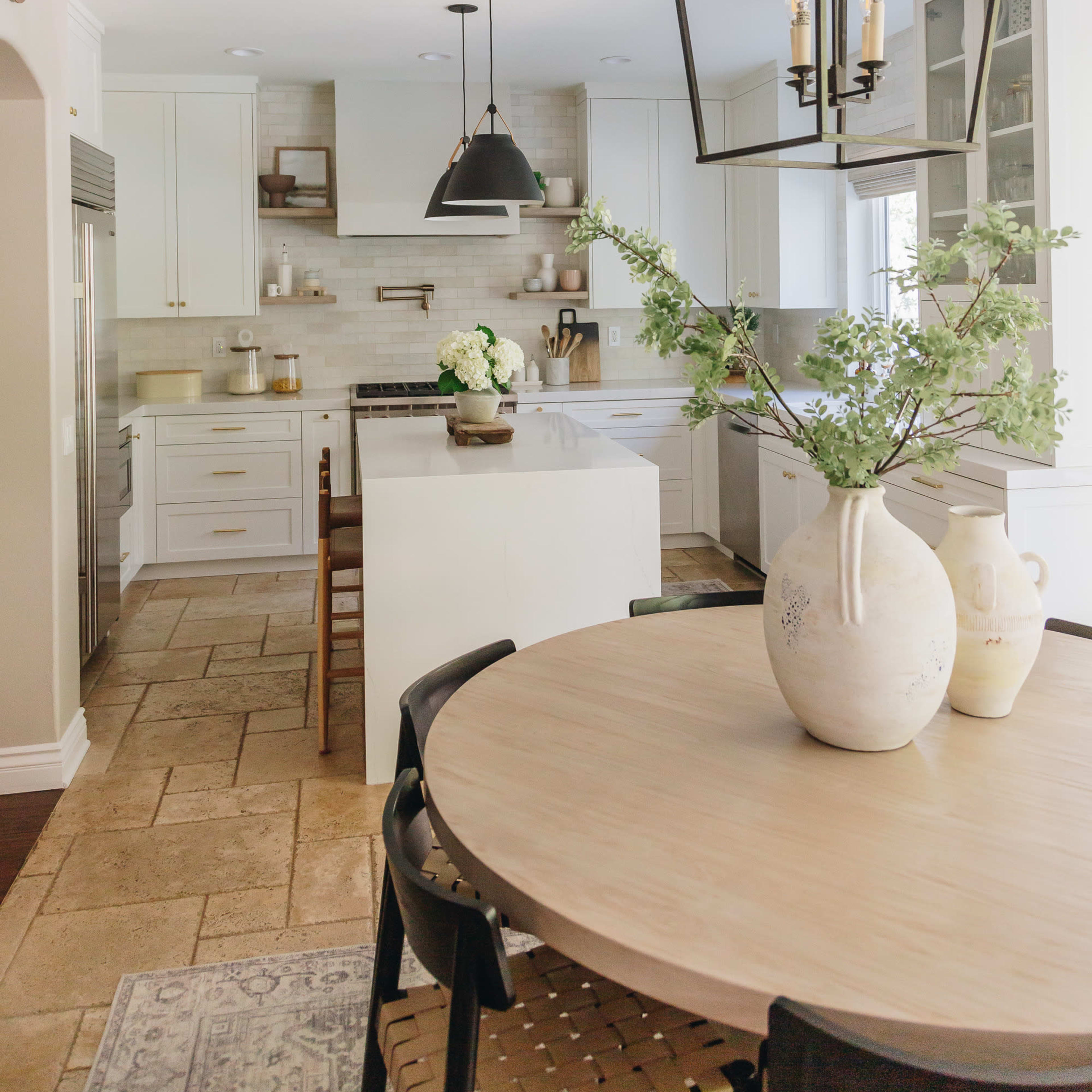 A bright, modern kitchen features white cabinetry, a large island, and a dining table surrounded by black chairs.