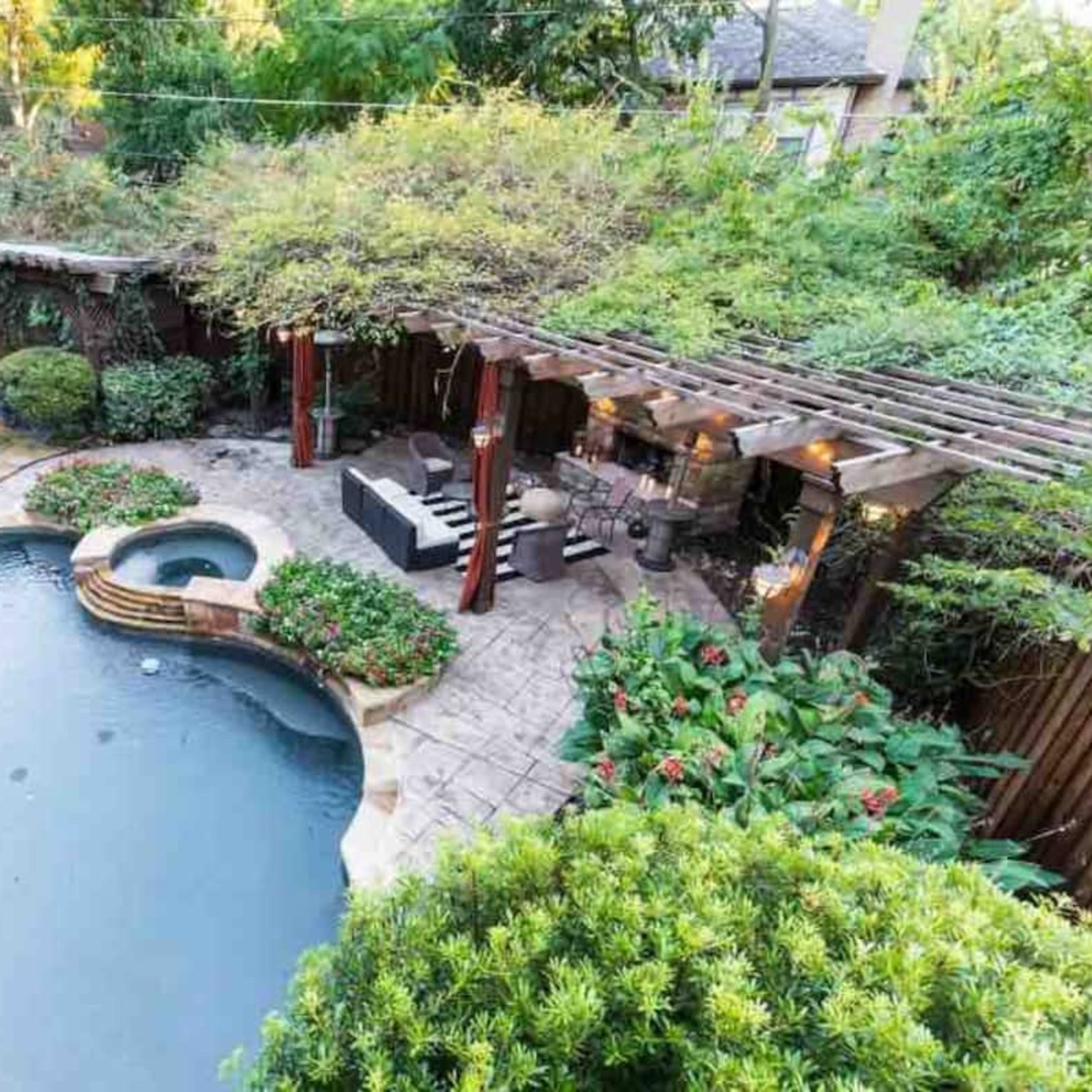 A backyard with a swimming pool, a spa area, stone patio, lounge chairs, and a shaded pergola surrounded by lush greenery.