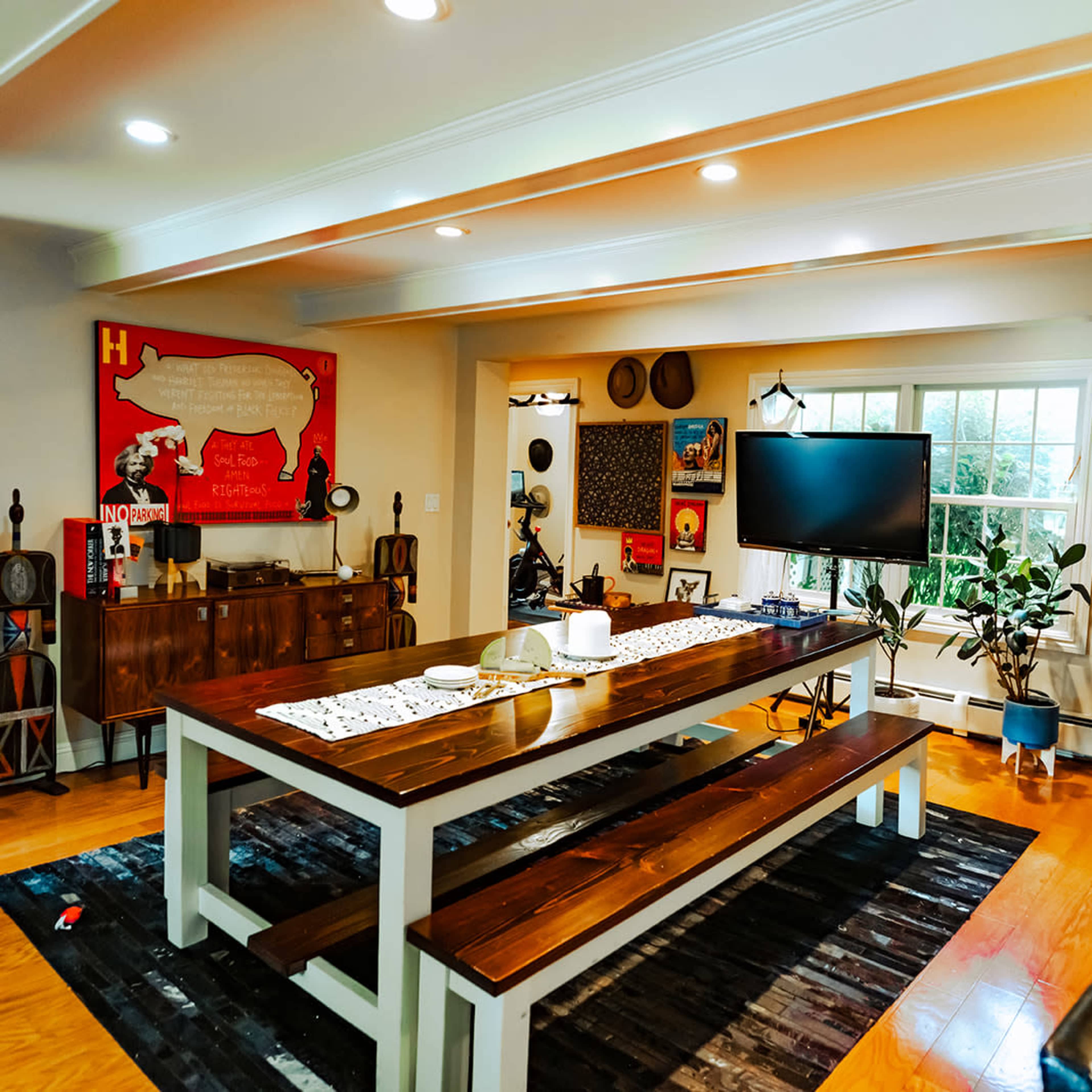 A modern dining area with a long wooden table, surrounded by black chairs, and large windows overlooking a garden.