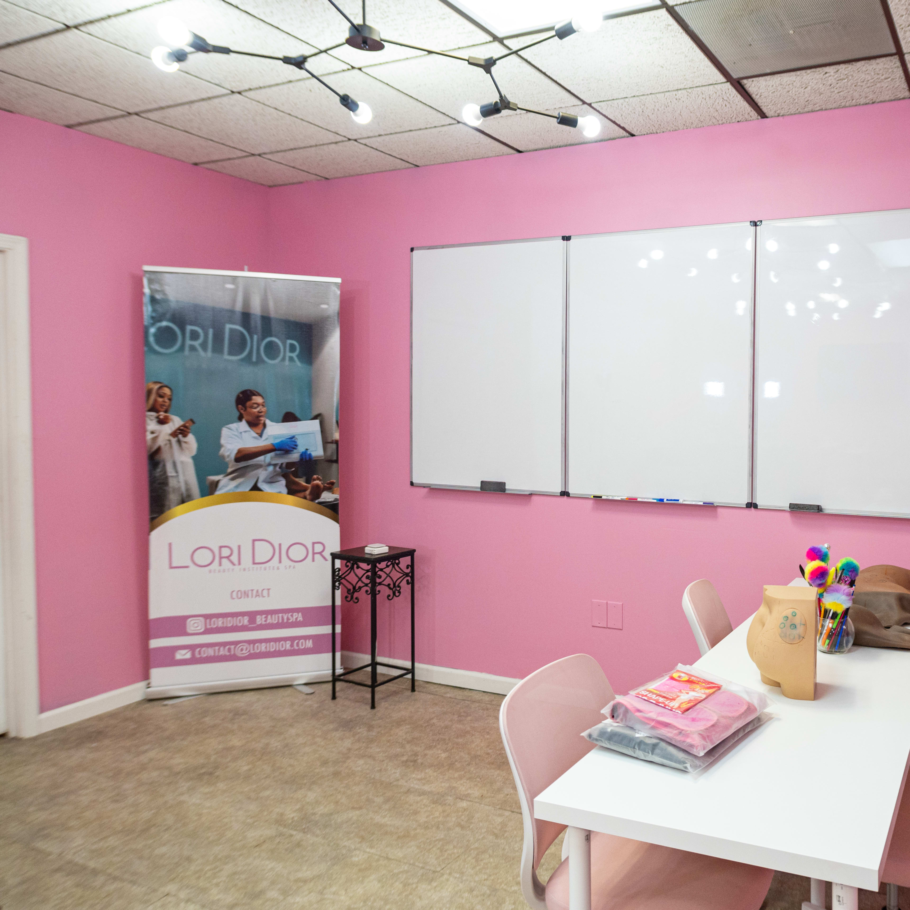 A brightly colored pink meeting room features a whiteboard, a table with chairs, and a promotional banner for Lori Dior.