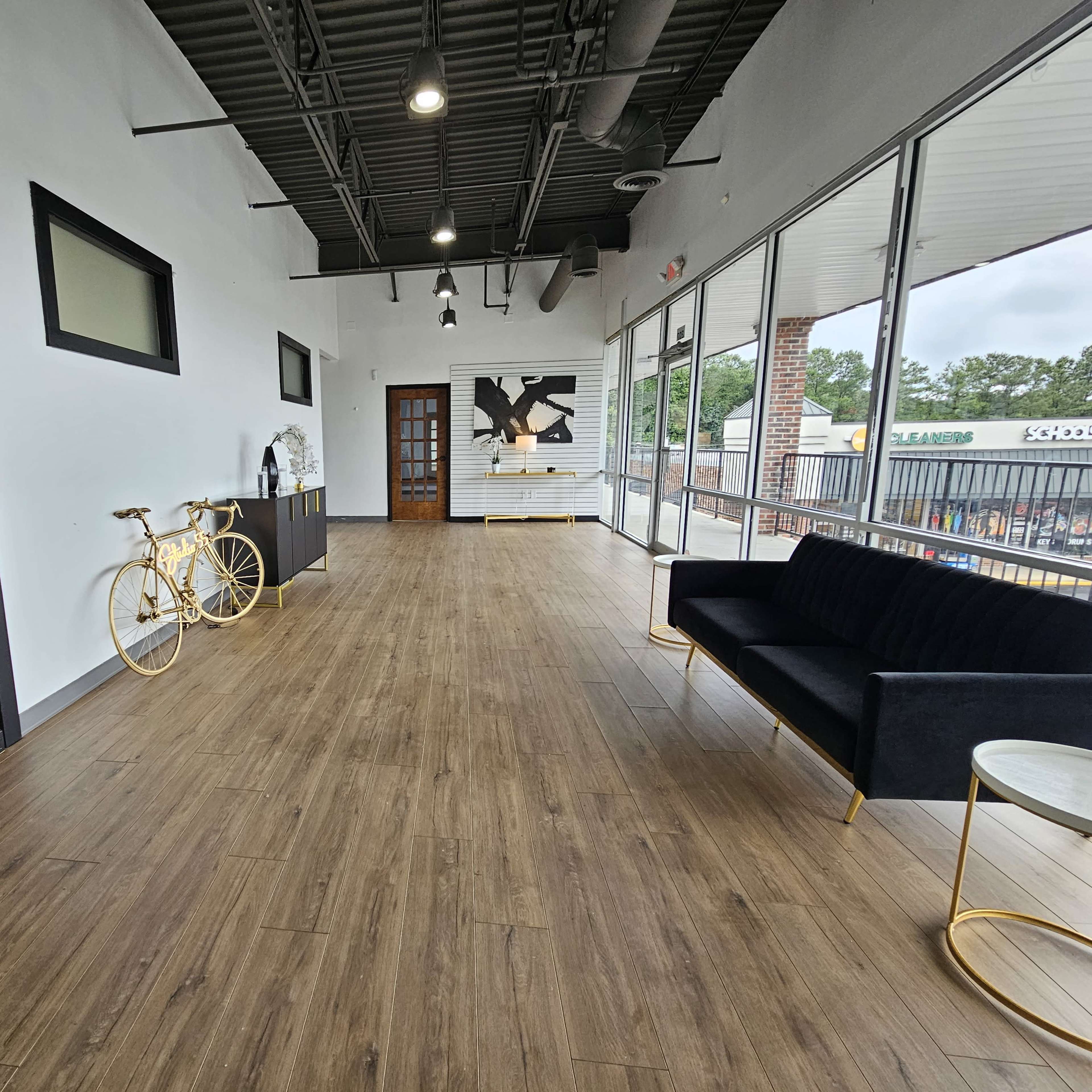 A spacious, modern interior with a wooden floor, two large black doors, a black couch, a small circular table, and a decorative yellow bicycle against the wall.