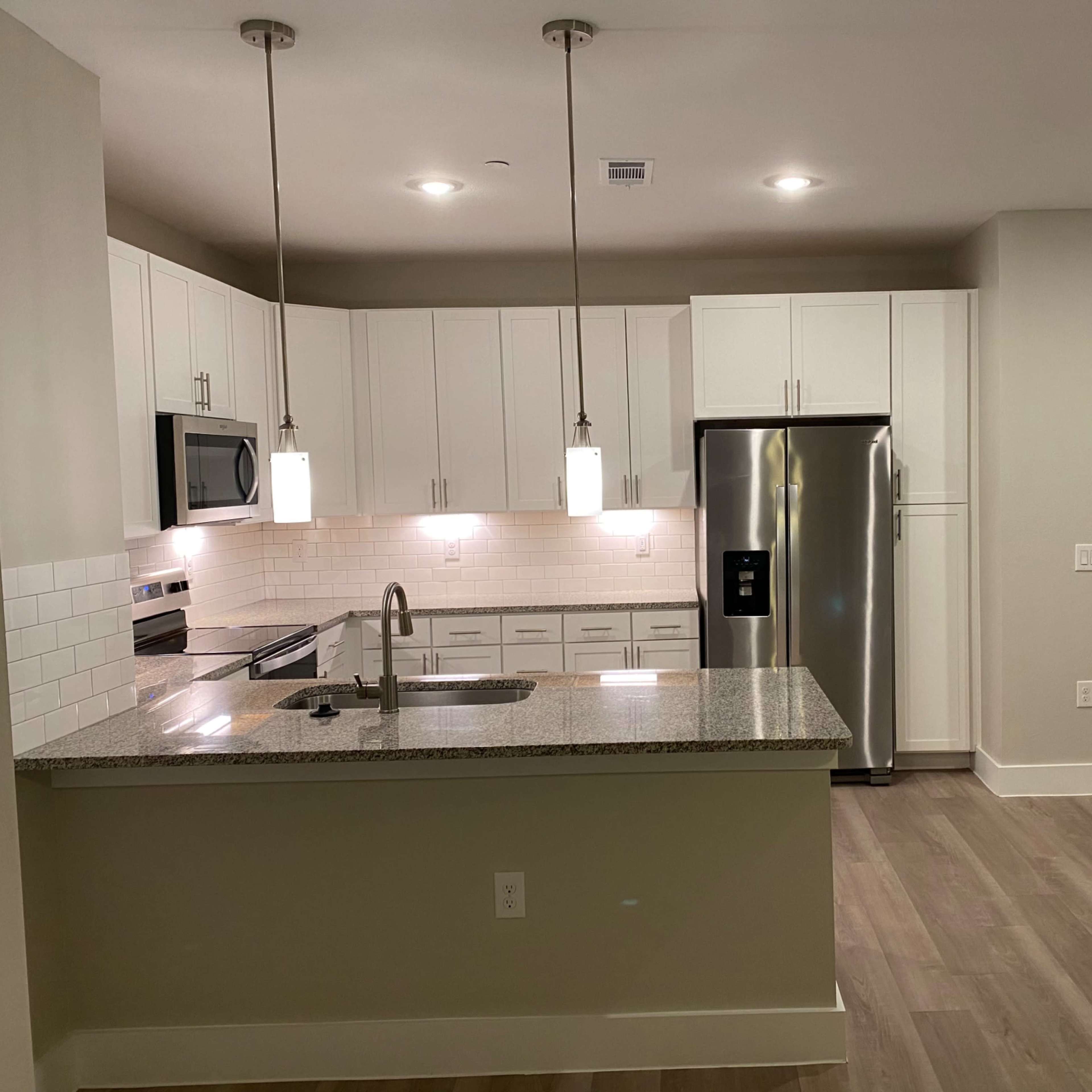 A modern kitchen features white cabinetry, stainless steel appliances, and a granite countertop with pendant lighting.