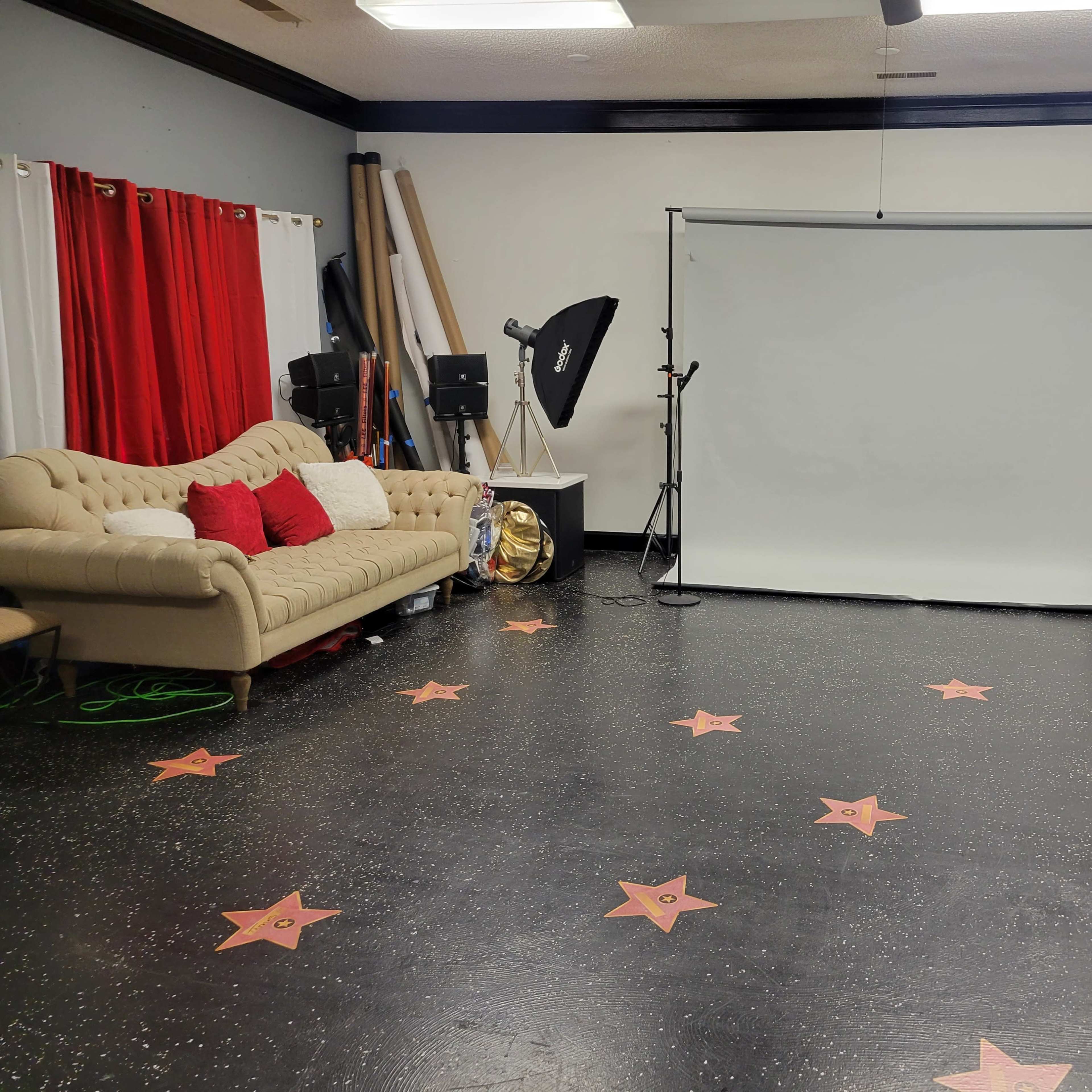 A photography studio with a beige couch, red curtains, a white backdrop, and a floor decorated with star-shaped designs.