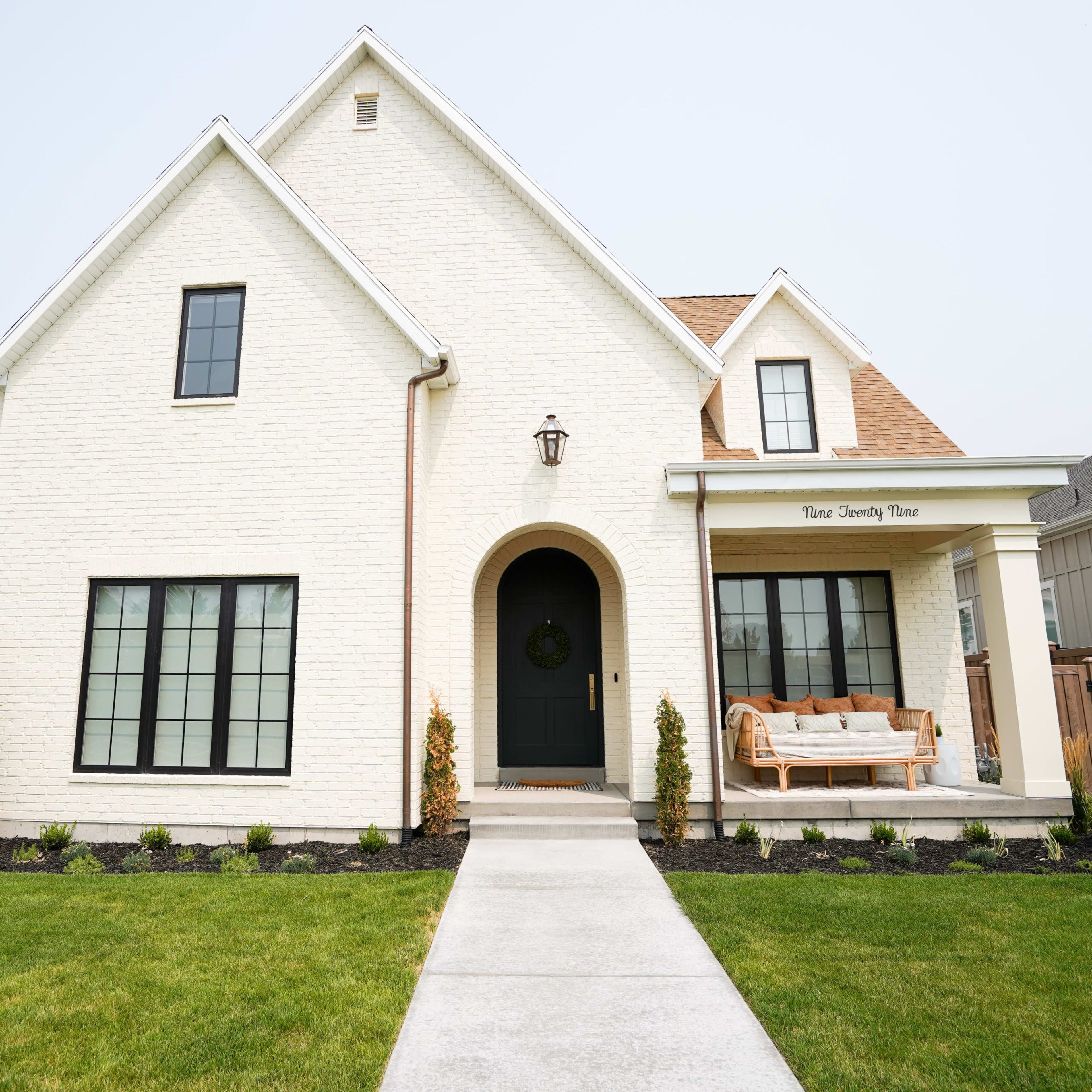 A white brick house features a welcoming front porch with a swing and neatly landscaped yard.
