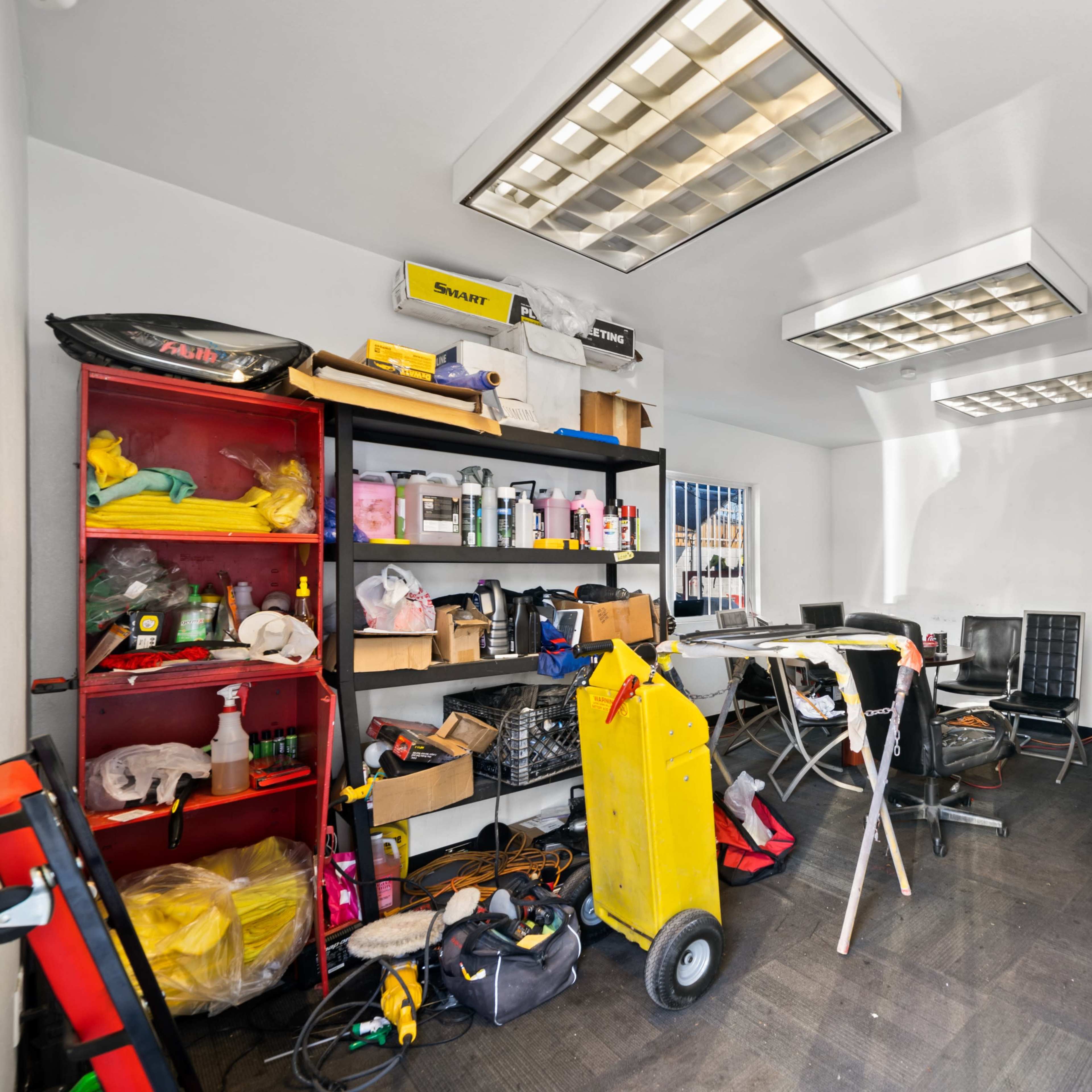A cluttered utility room with shelves filled with cleaning supplies, tools, and a rolling cart in the center.