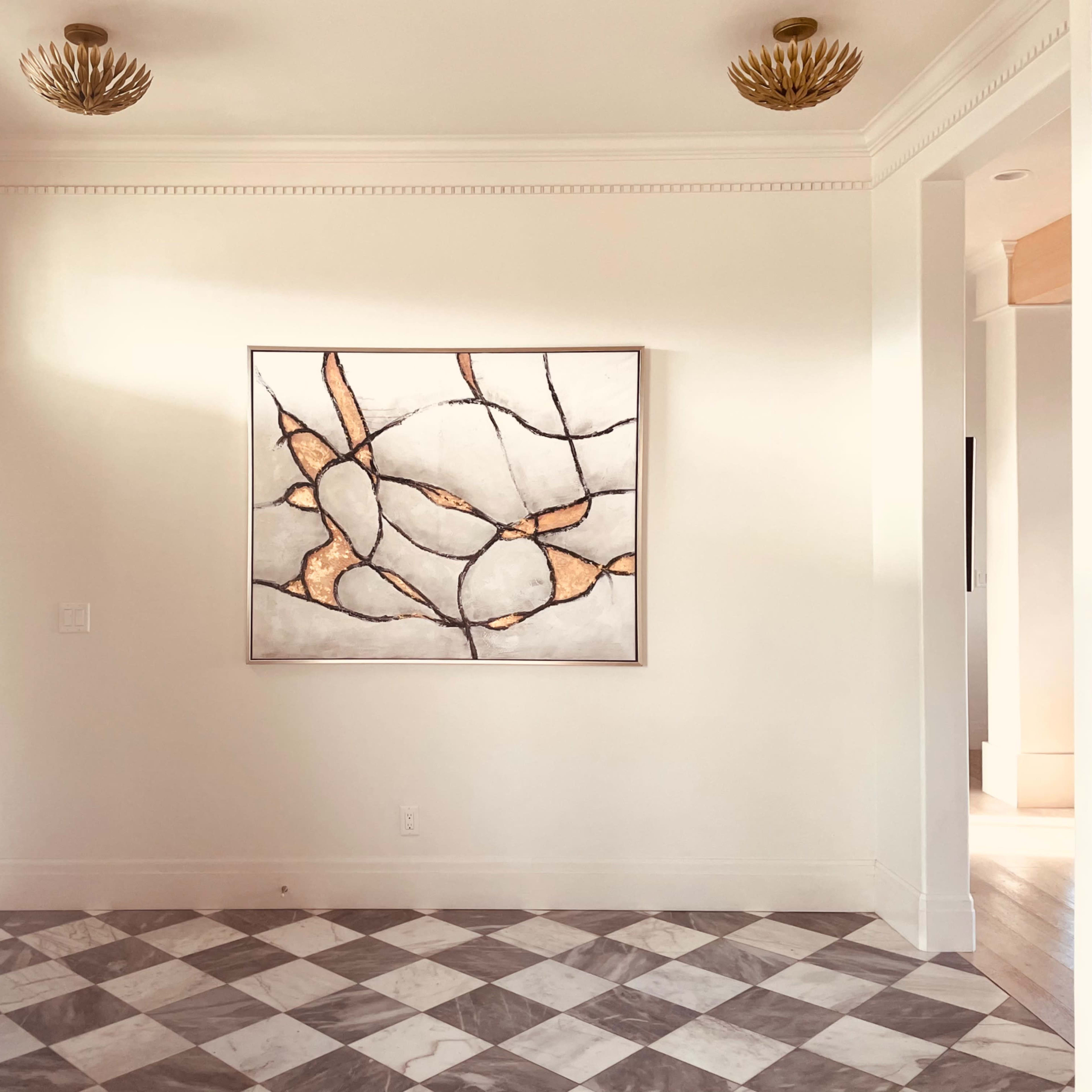A spacious entryway with a geometric art piece mounted on a light-colored wall above a checkered floor.