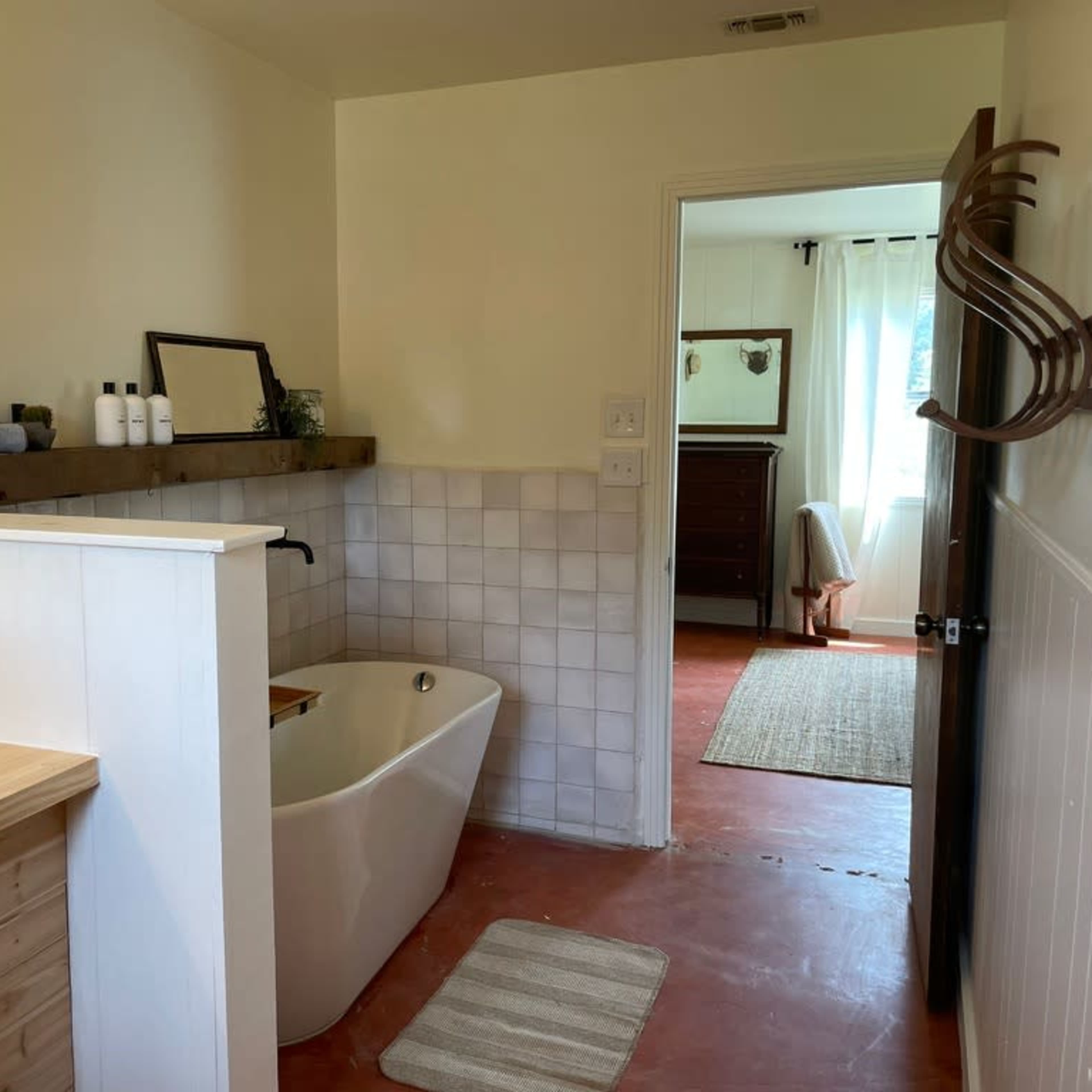 A bathroom featuring a freestanding bathtub, a wooden vanity with a sink, and a doorway leading to another room.
