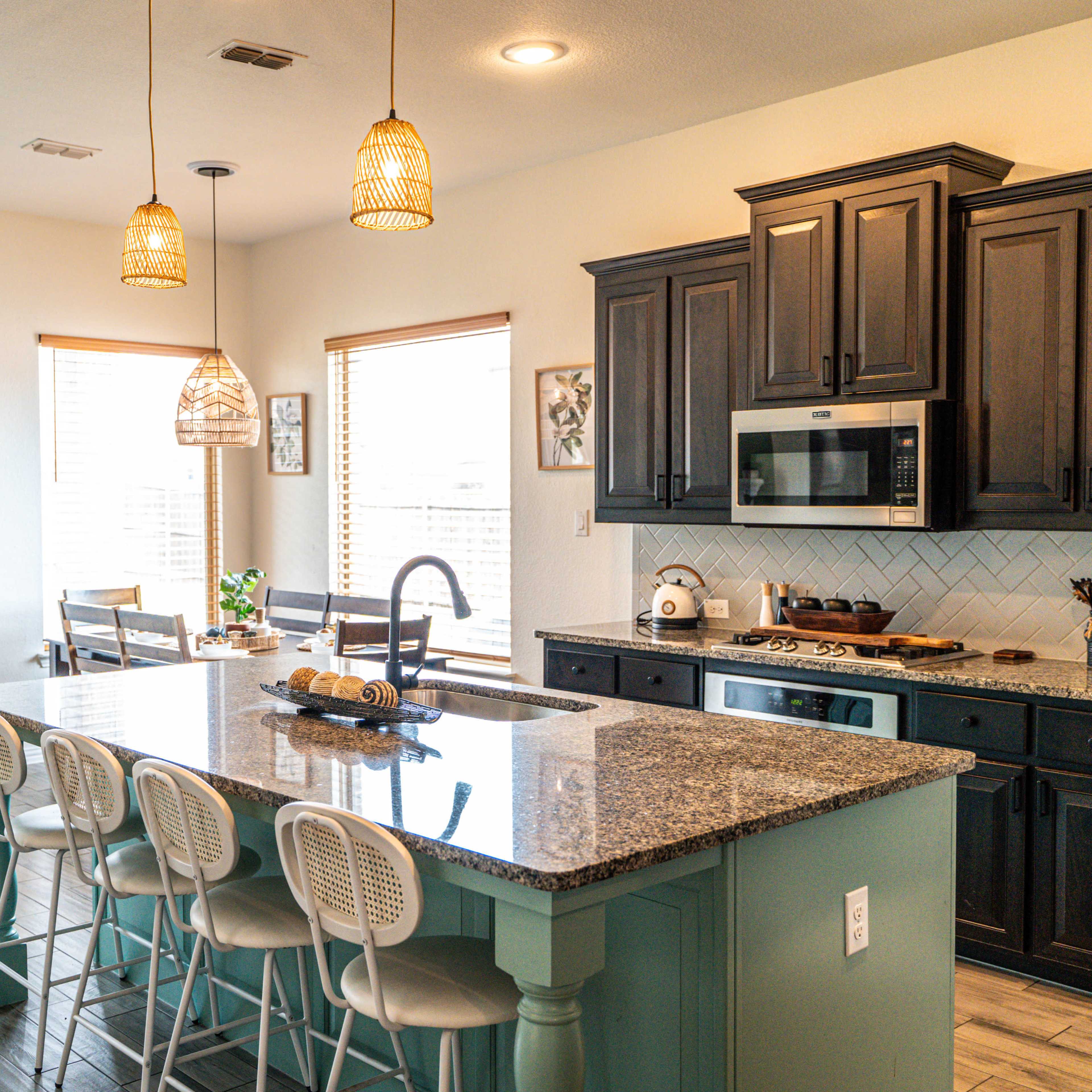 A modern kitchen features dark wooden cabinets, a large island with seating, and pendant lights hanging above.