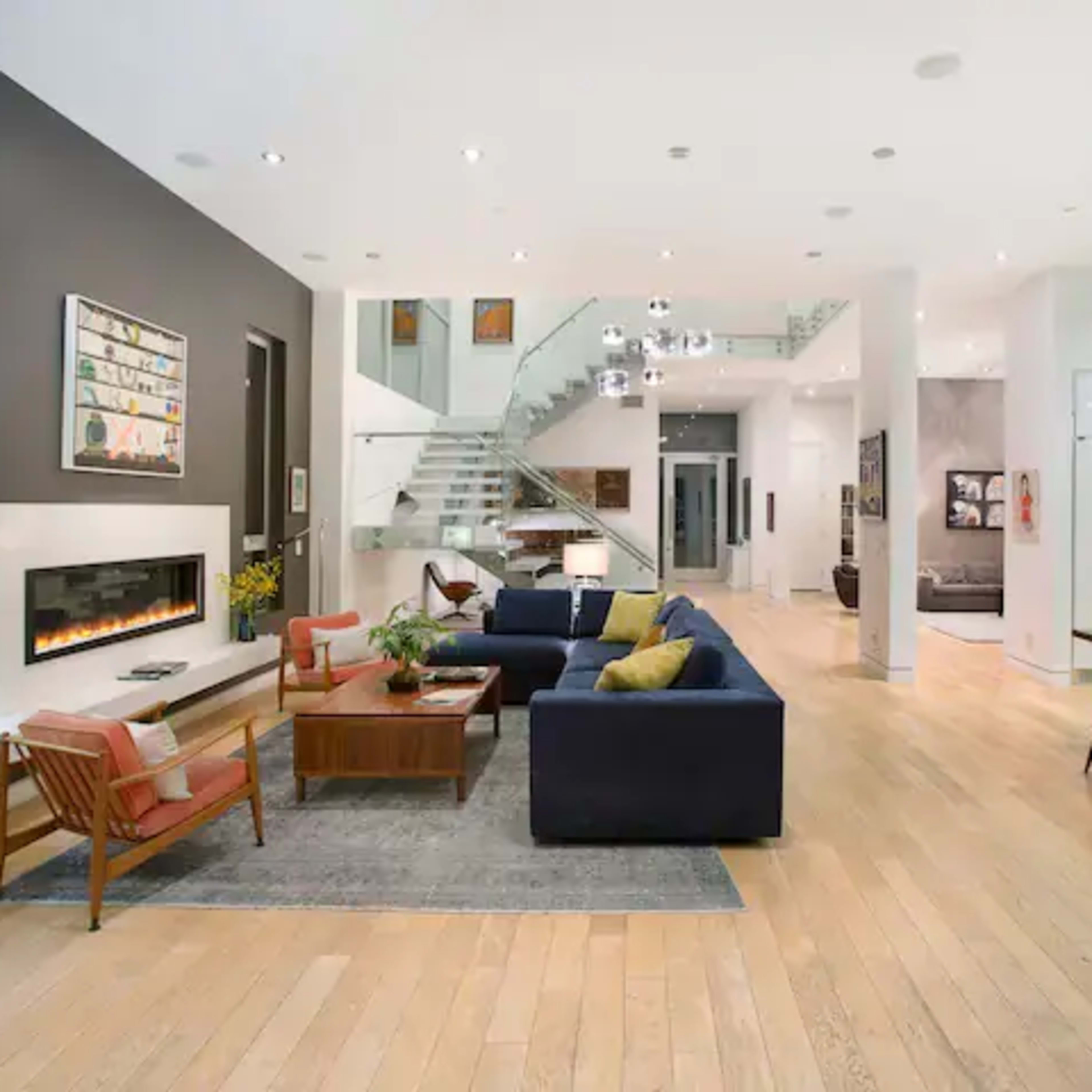 A spacious modern living room and dining area with hardwood floors, a fireplace, and a staircase leading to an upper level.