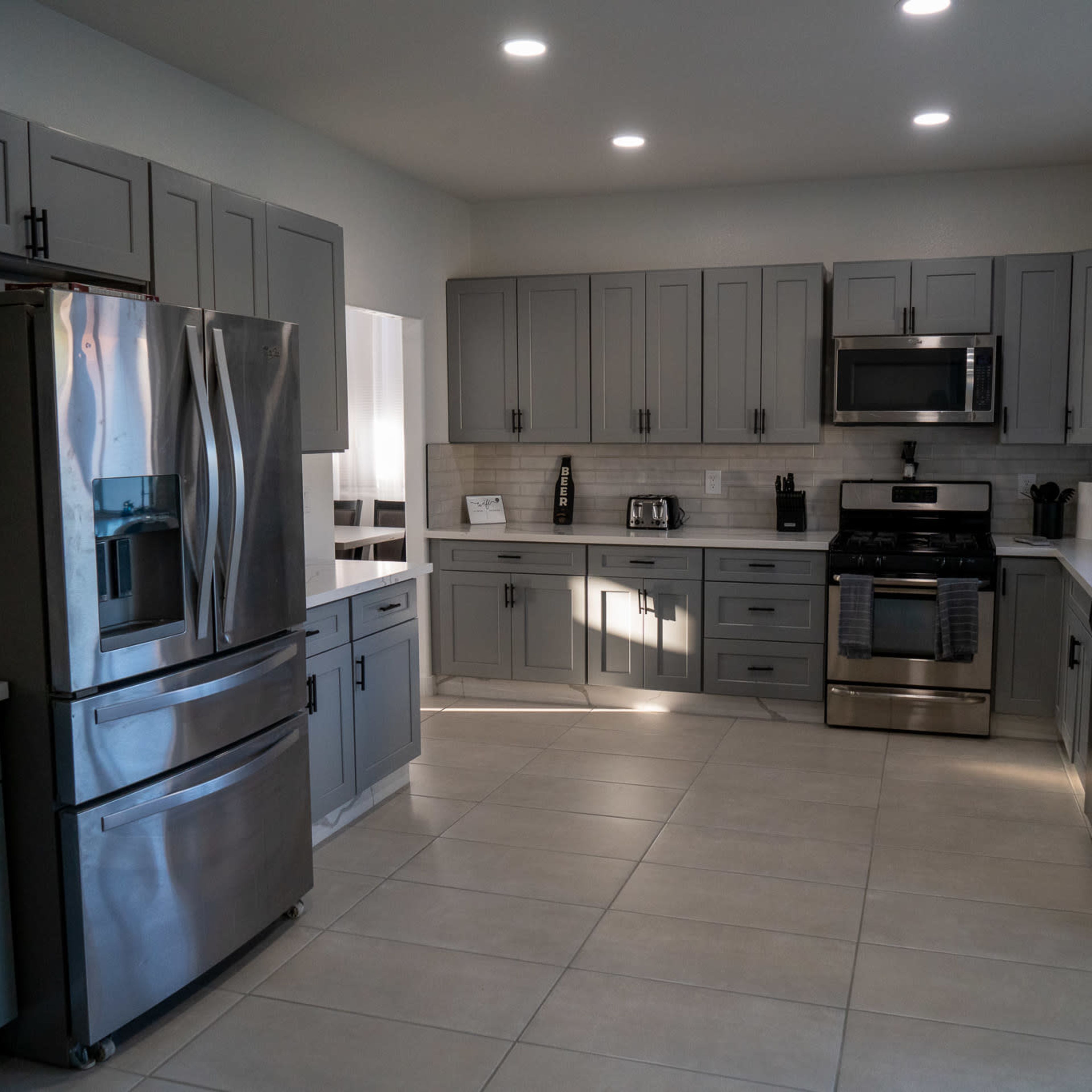 A modern kitchen with gray cabinets, stainless steel appliances, and a tiled floor.