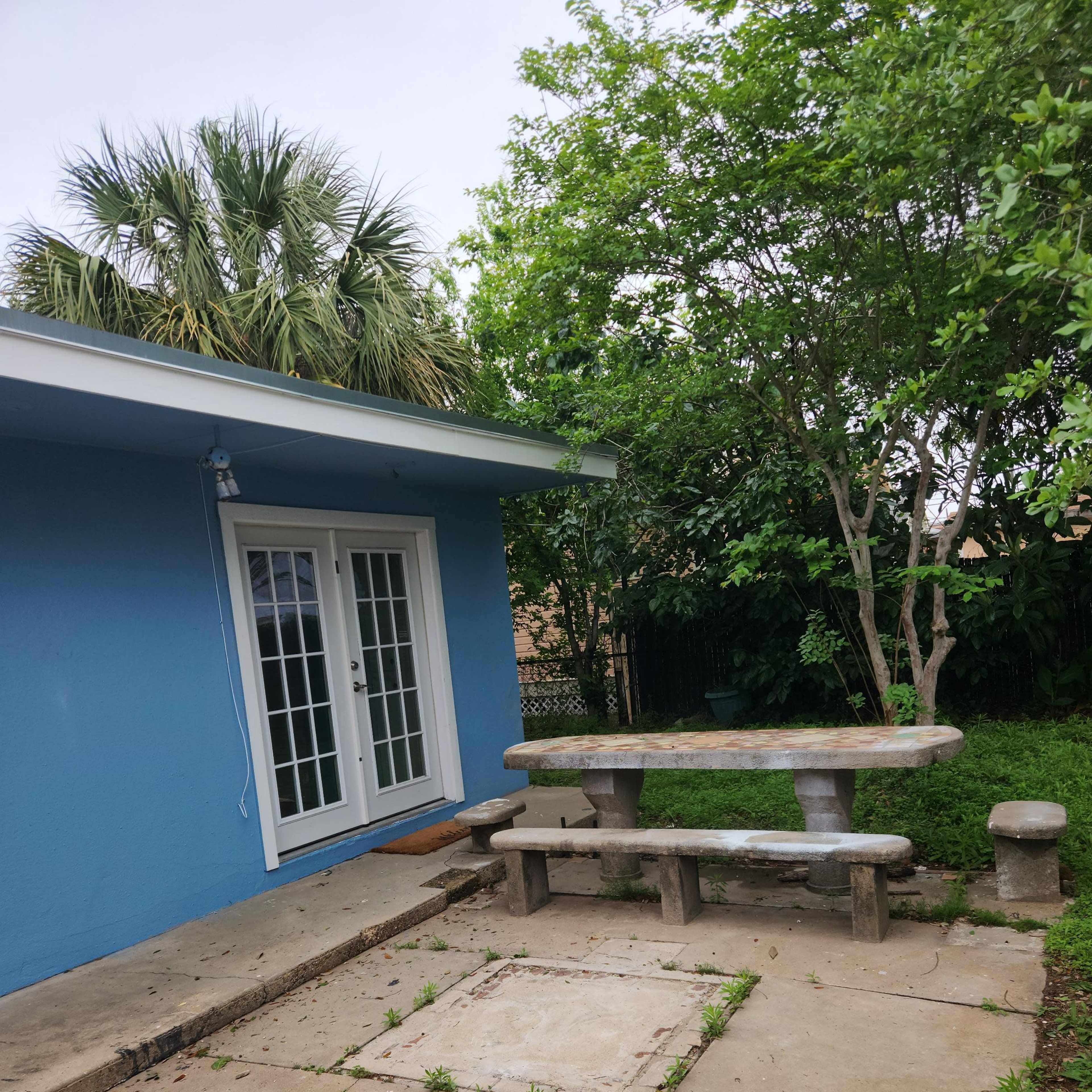 A blue house with a patio area featuring a stone table and benches surrounded by greenery.