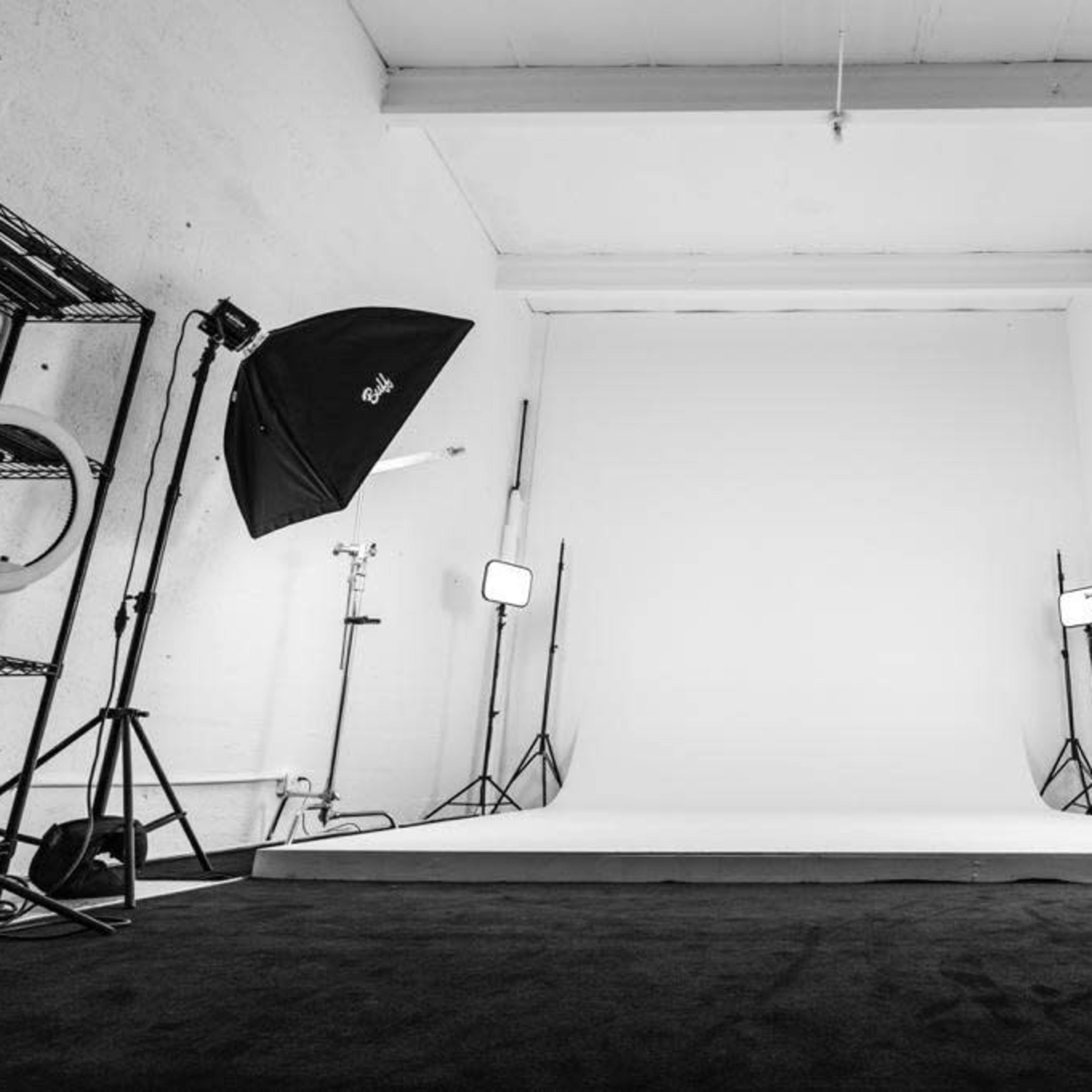 A photography studio features a blank backdrop surrounded by multiple lighting setups and a dark carpet.