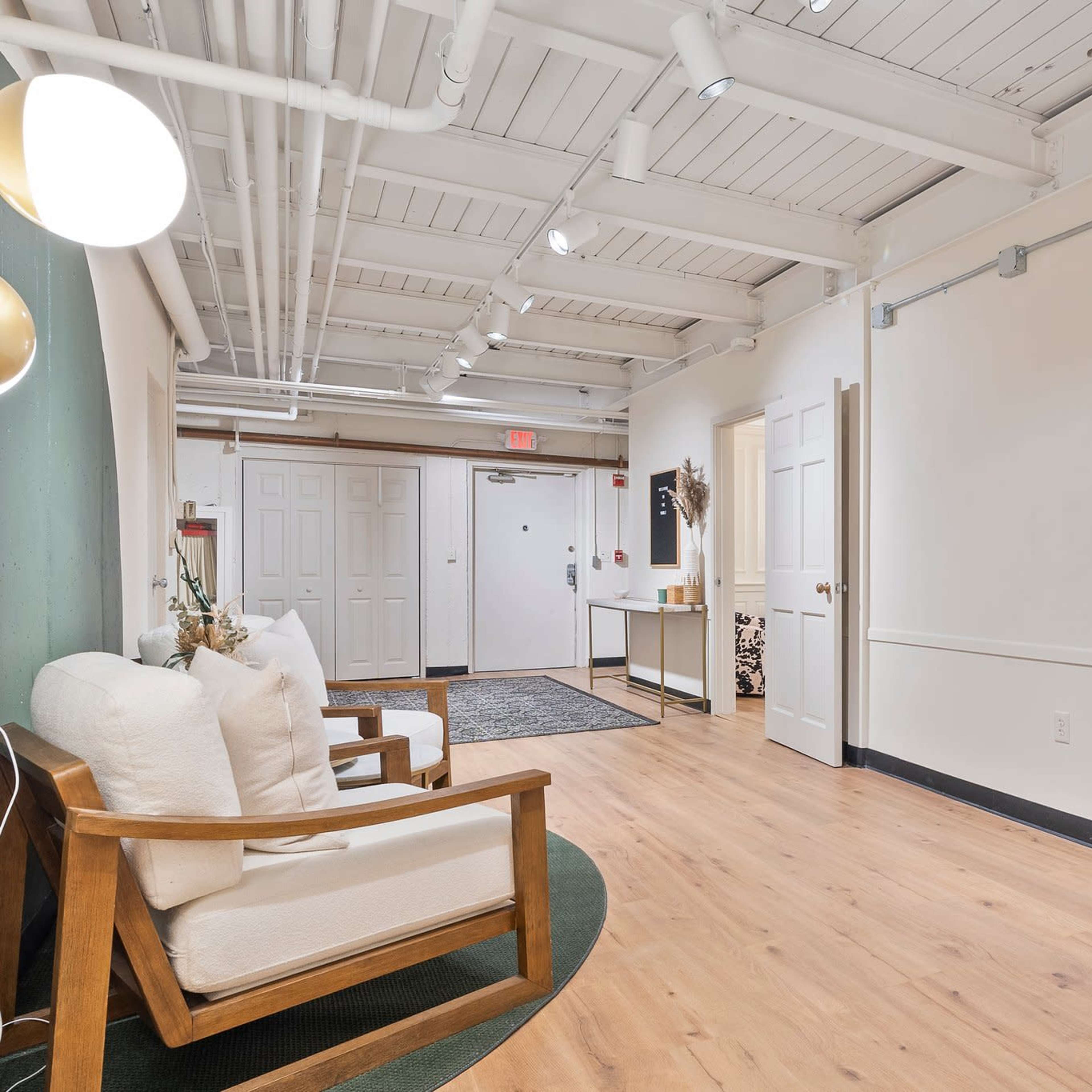 A spacious hallway with light wood flooring, two wooden chairs, and a closed door at the end.