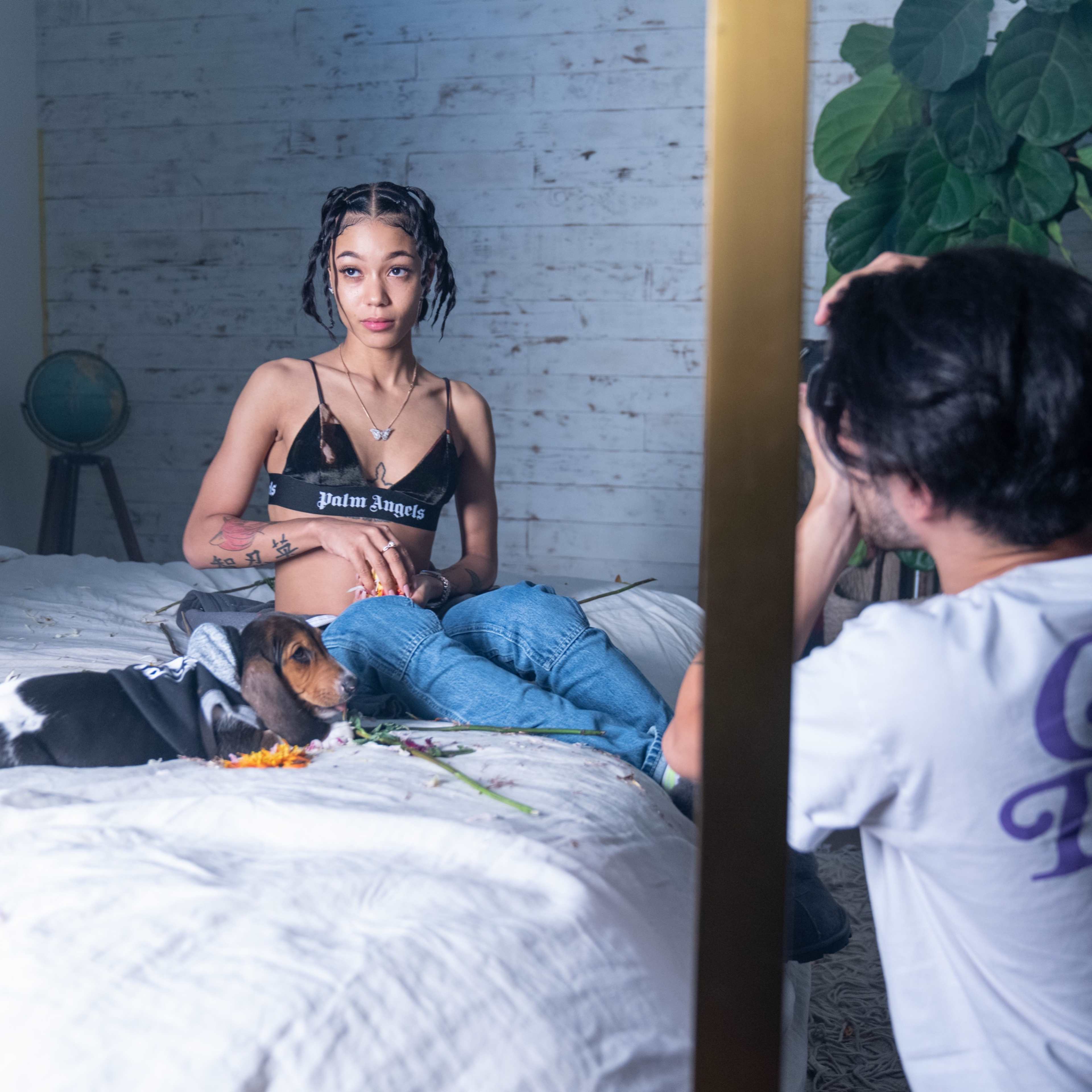 A woman sits on a bed with a dog beside her while a photographer captures the scene.