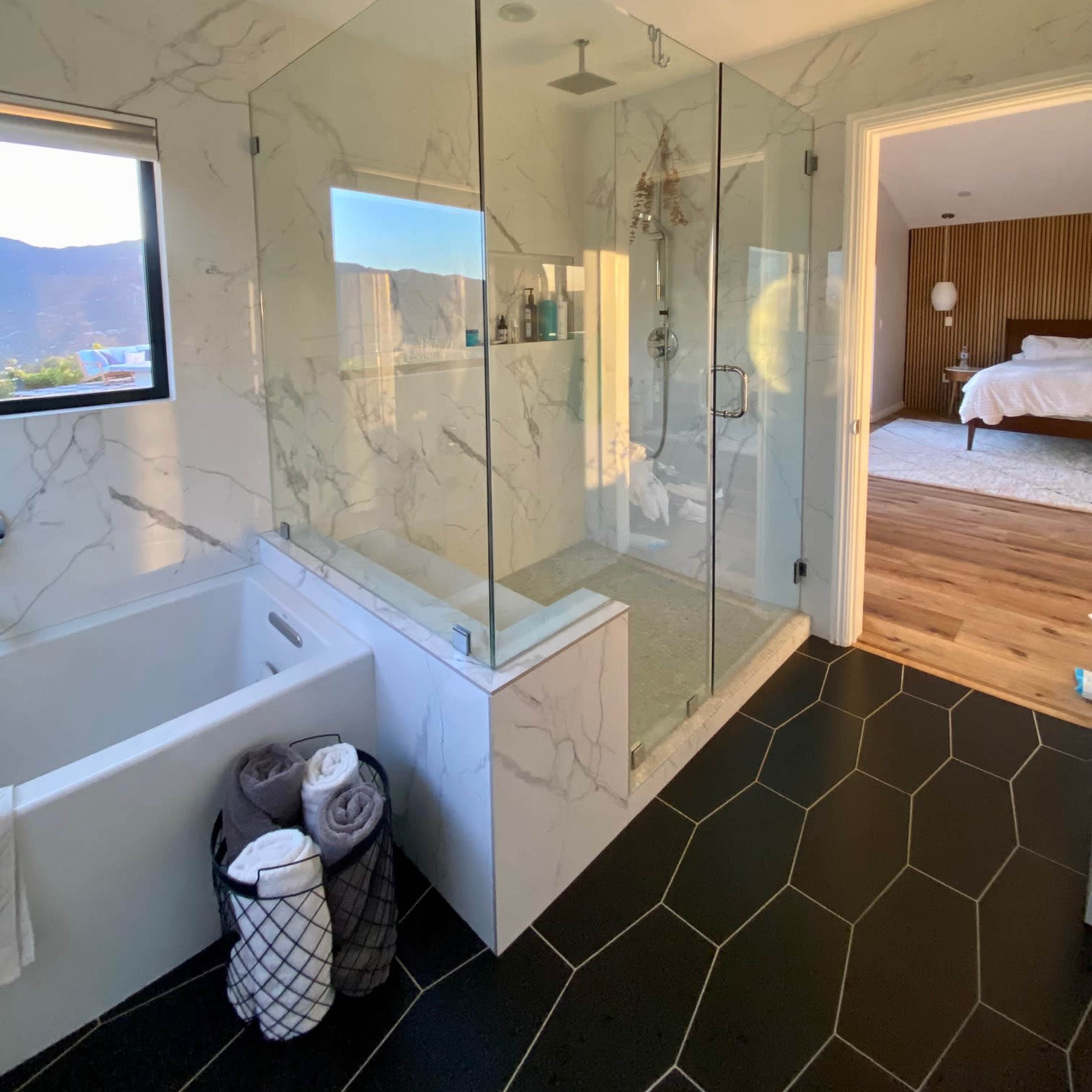 A modern bathroom featuring a glass shower enclosure, a freestanding bathtub, and a spacious layout with natural light.