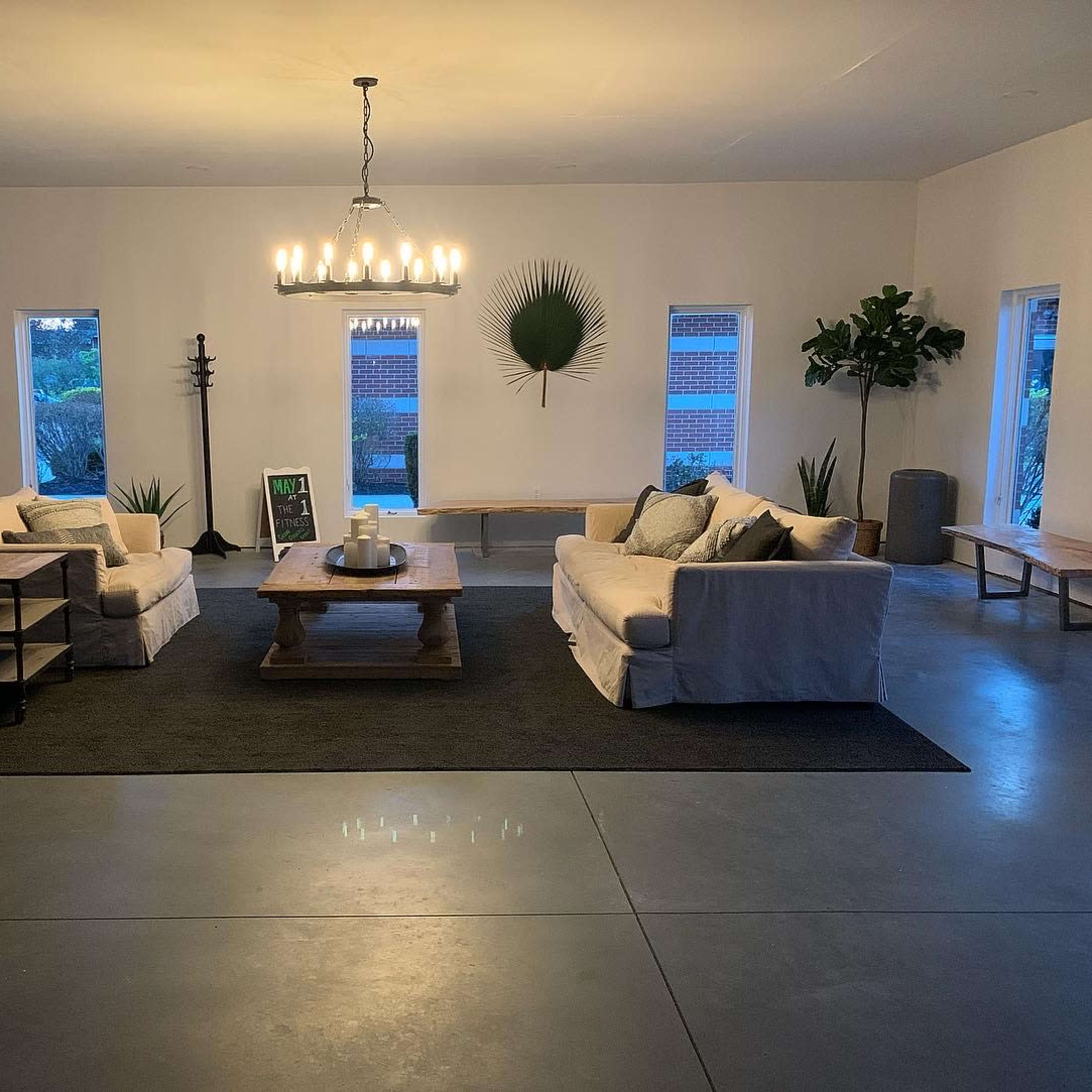 A spacious living room features two sofas facing a wooden table, with large windows and decorative plants accentuating the minimalist design.