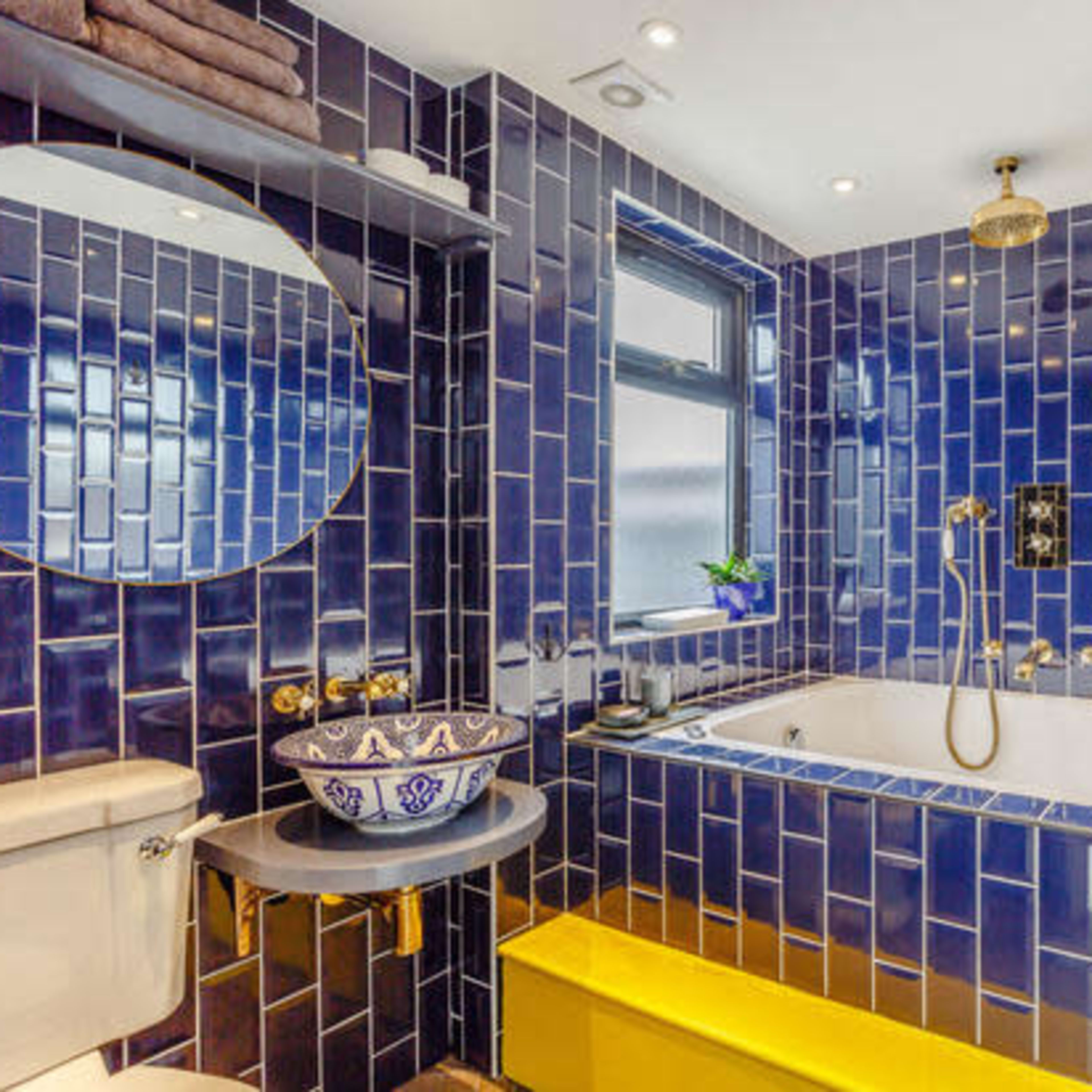 A modern bathroom featuring blue tiled walls, a soaking tub, and a yellow accent piece.