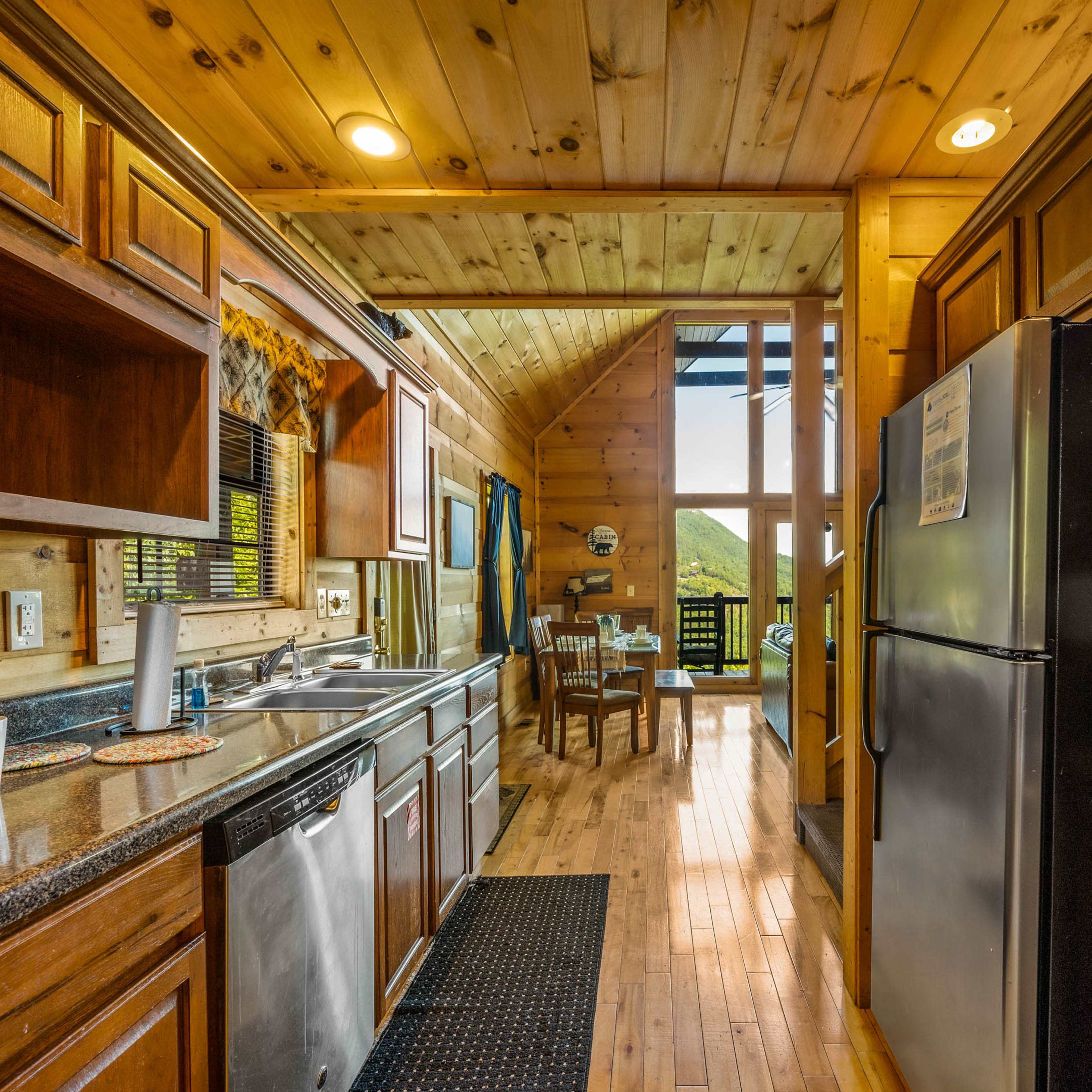 A wooden kitchen with stainless steel appliances, a view of a dining area, and large windows overlooking a mountain landscape.