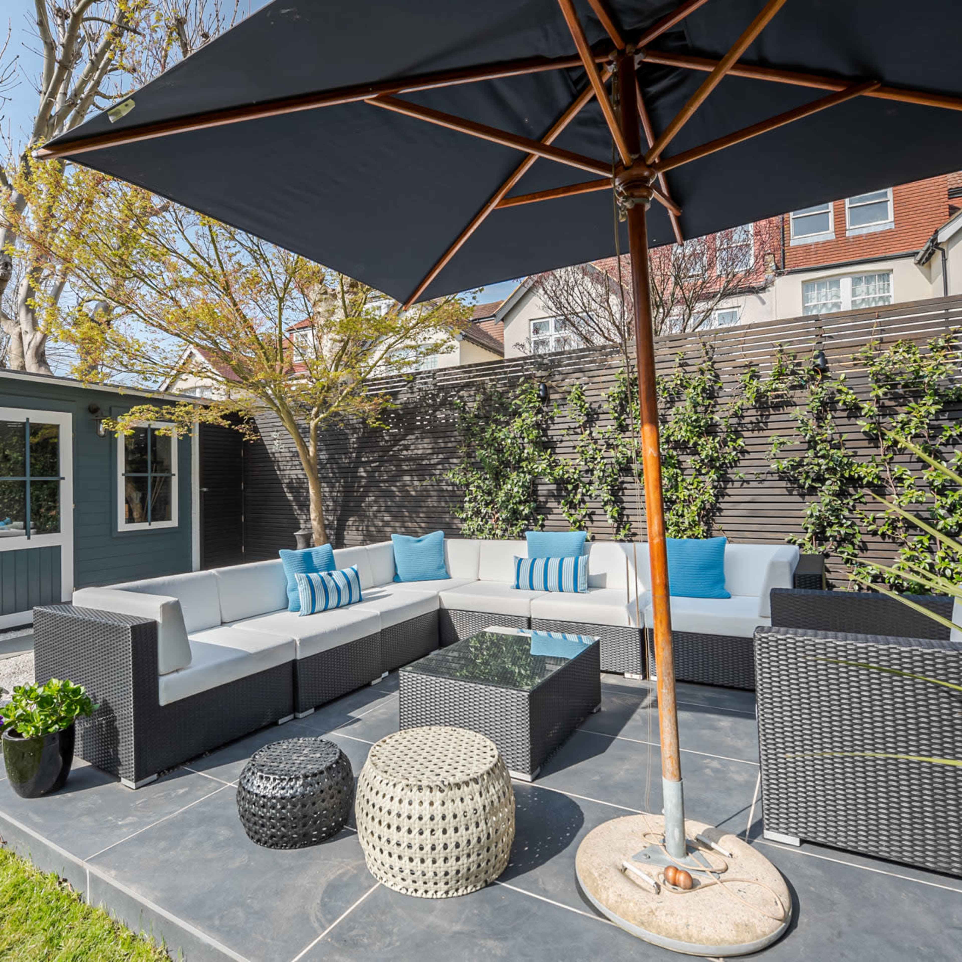 A cozy outdoor seating area with a sectional sofa, an umbrella, and a garden shed surrounded by greenery.