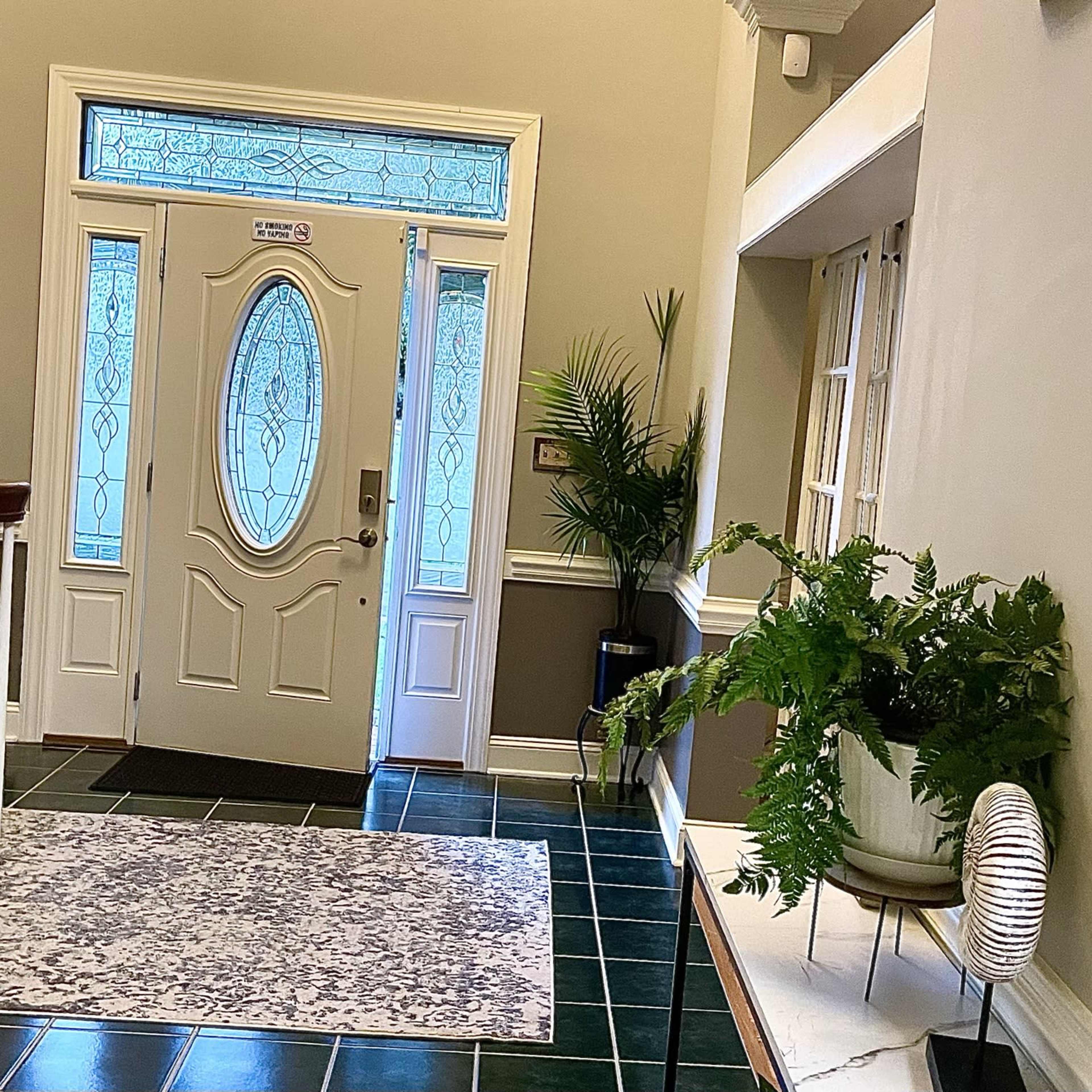 An interior entrance hall with a decorative rug, a doorway with stained glass, and a potted plant on the side.