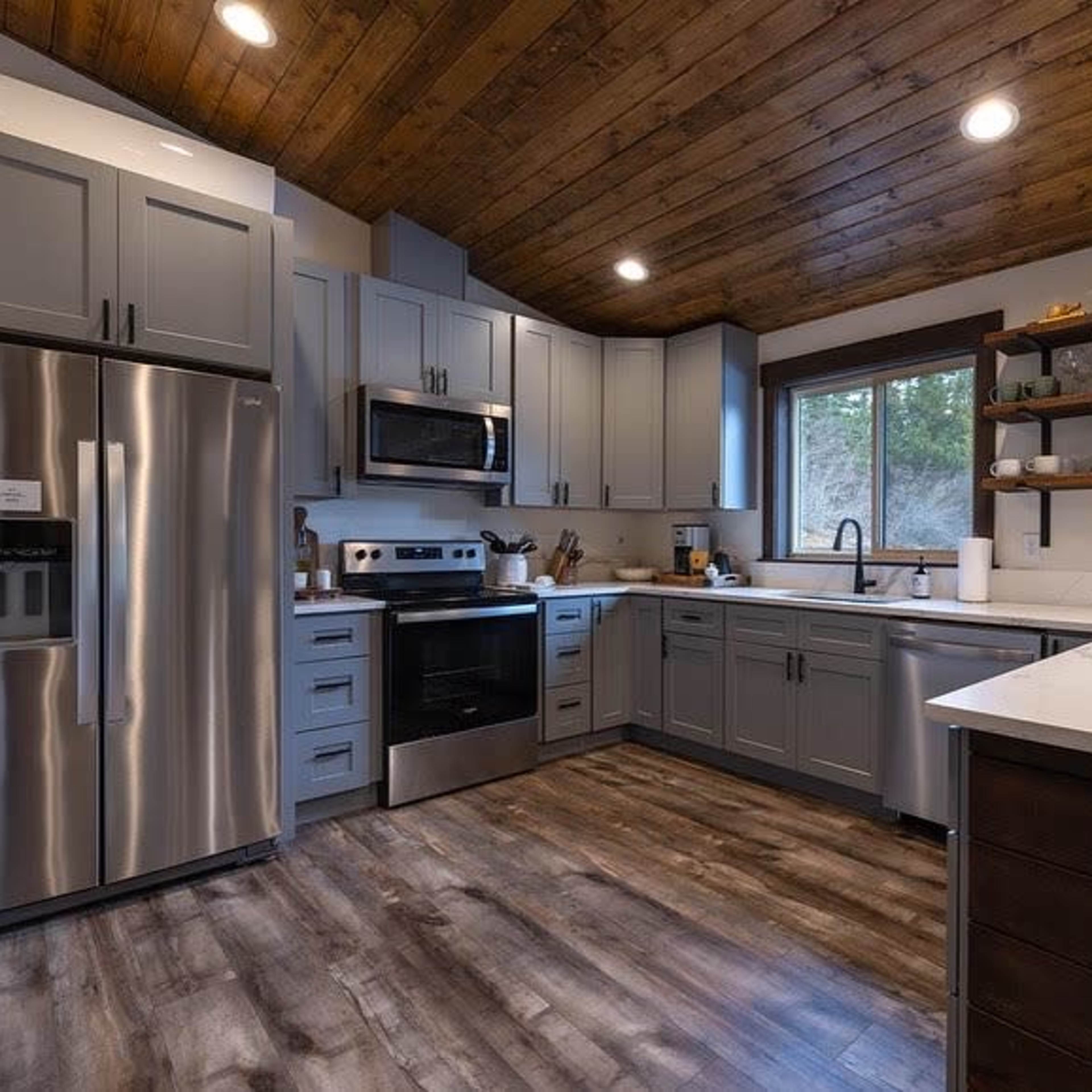 A modern kitchen features stainless steel appliances, gray cabinetry, and a wooden ceiling with open shelves displaying dishware.