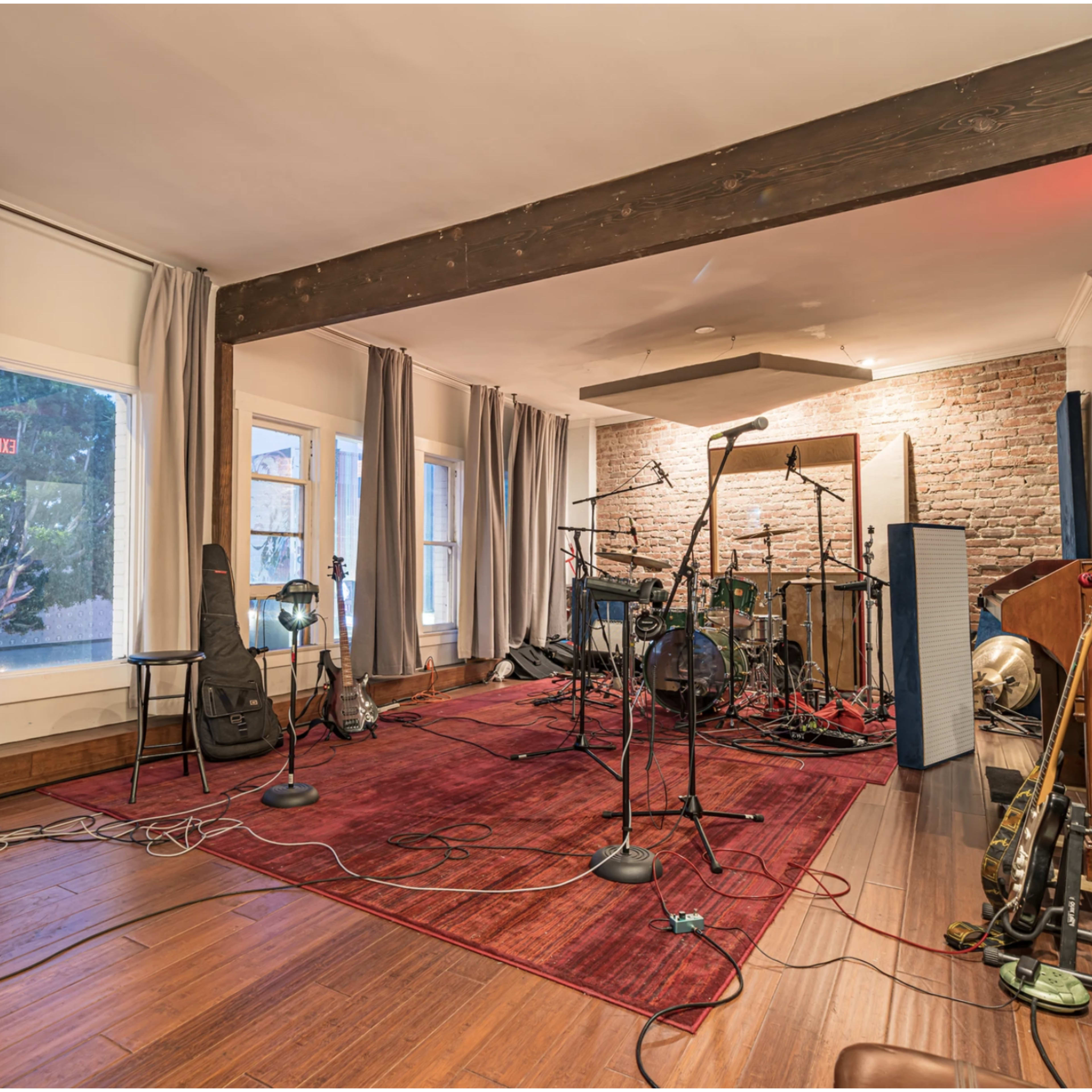 A music studio features instruments, microphones, and a carpeted area under natural light from large windows.