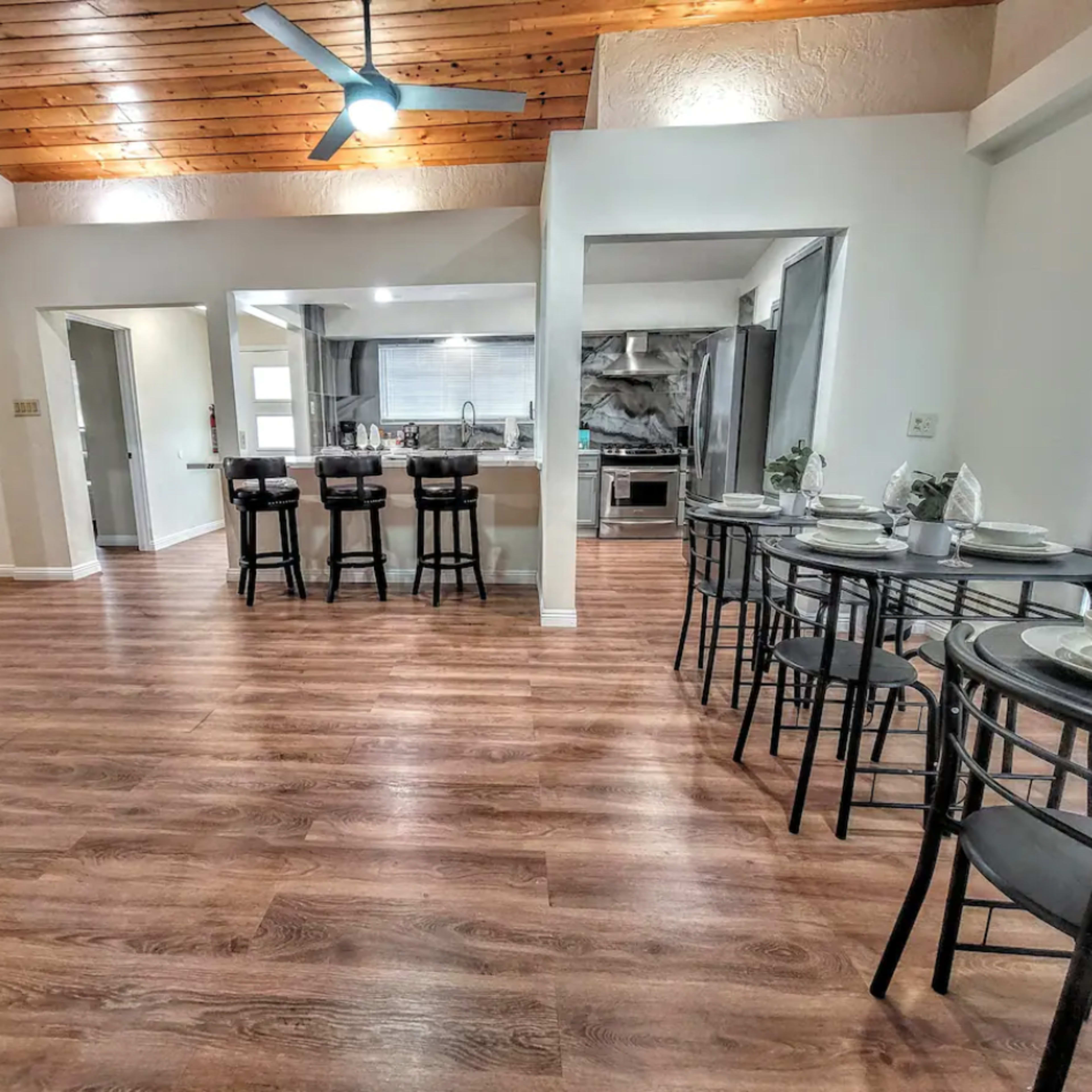 A spacious interior features wooden beams on the ceiling, a dining area with a round table, and a kitchen visible in the background.
