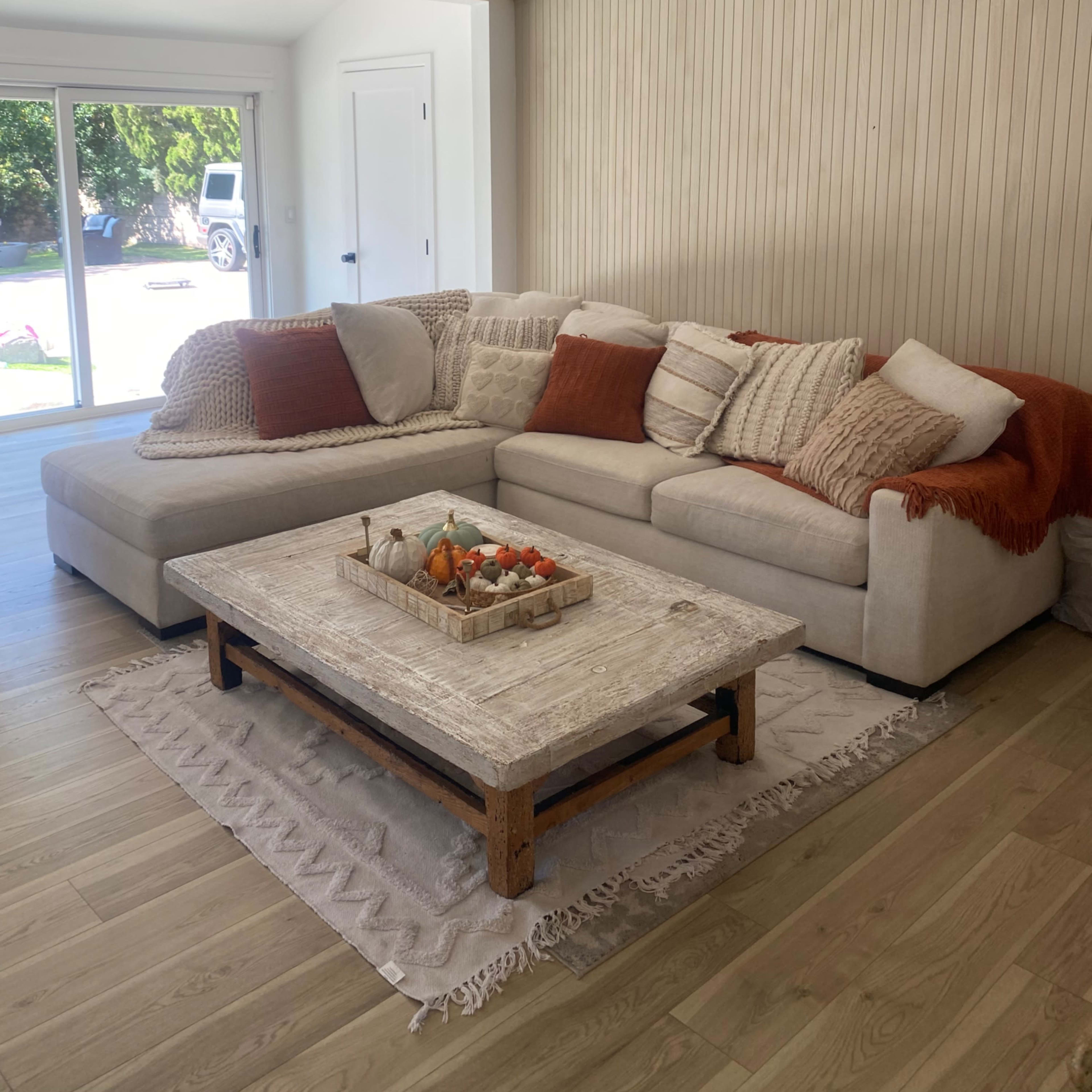A cozy living room featuring a sectional sofa with decorative pillows and a wooden coffee table decorated with a small tray of fruits.